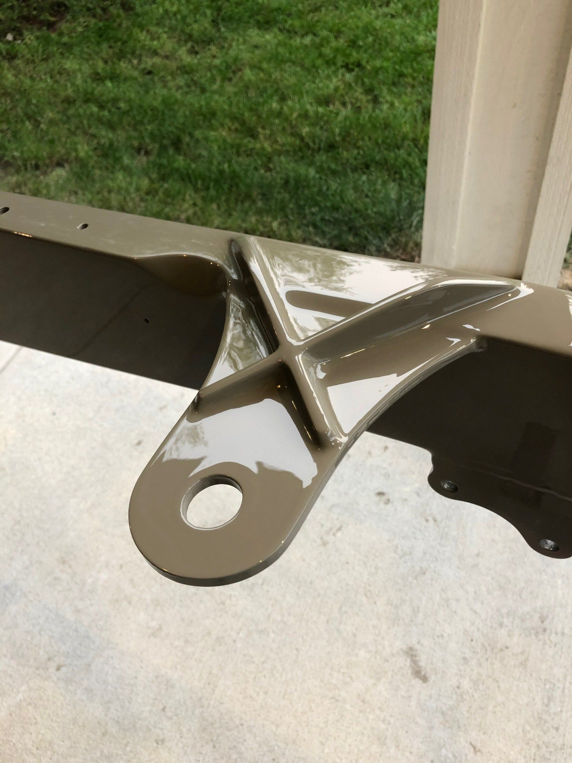 Broken metal bracket on concrete porch beside a white post and green grass.