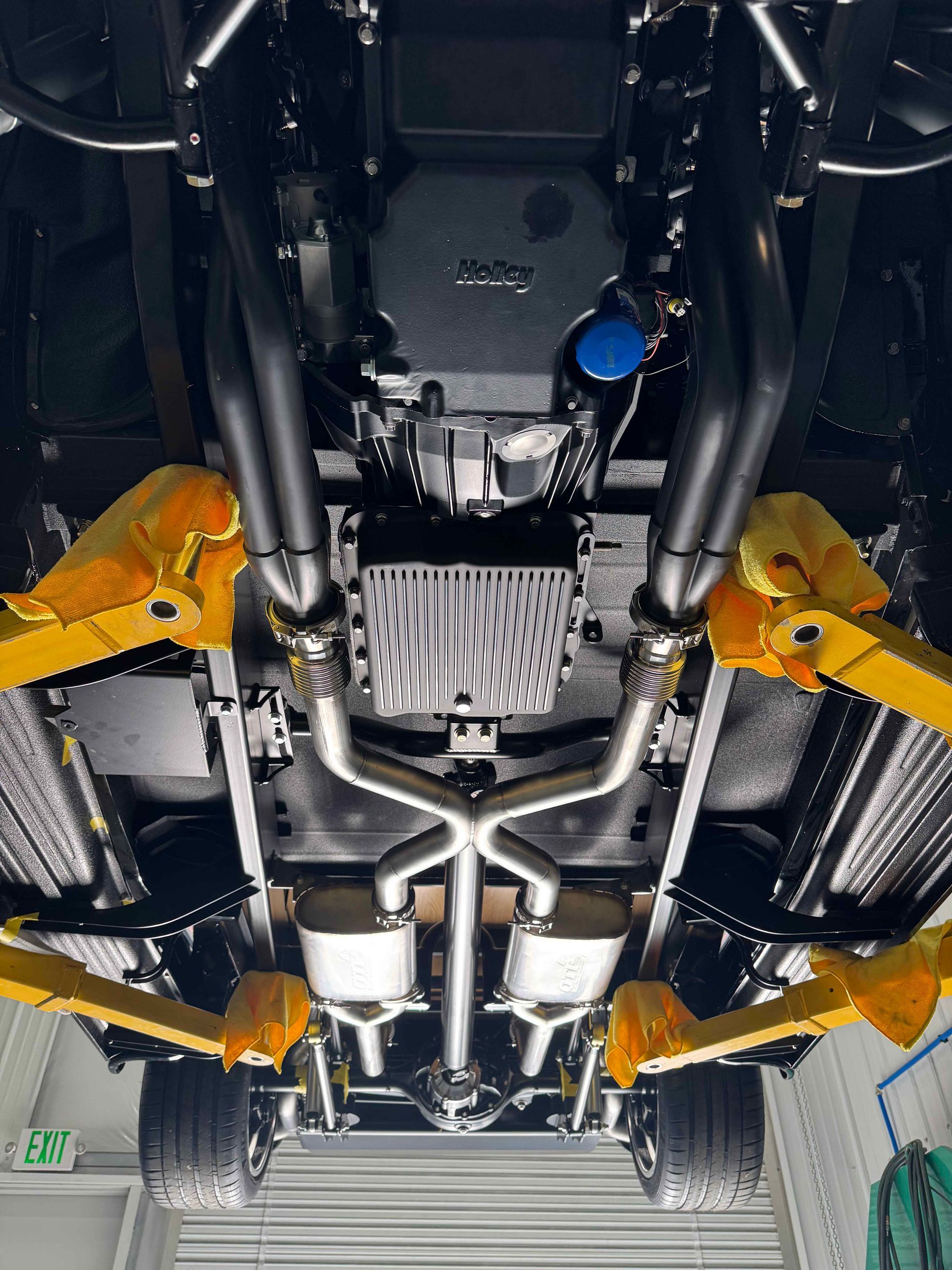 Undercarriage of a car on a lift, with yellow suspension arms and visible exhaust components.