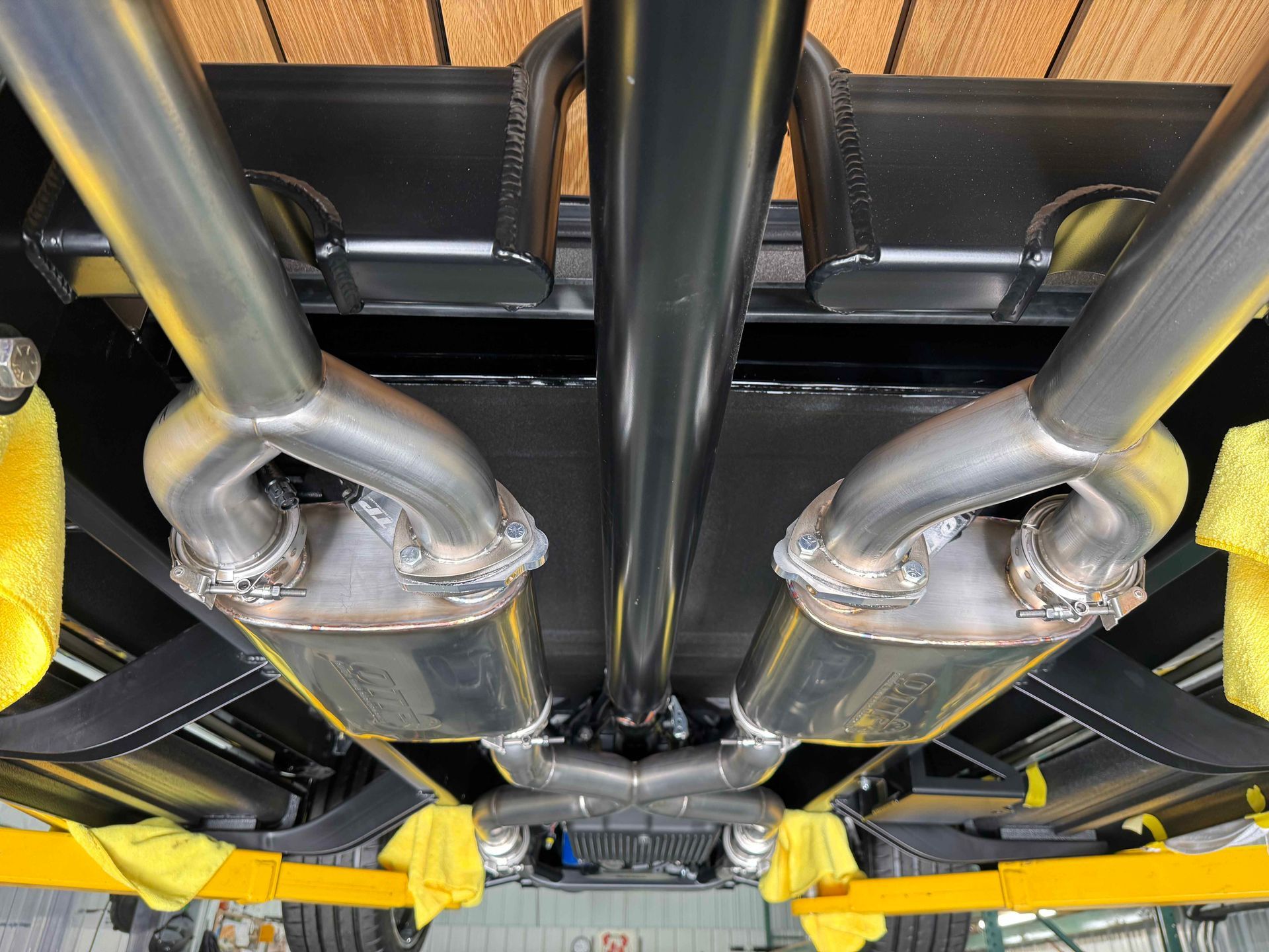 Underbody view of a vehicle with dual exhaust pipes and yellow suspension components