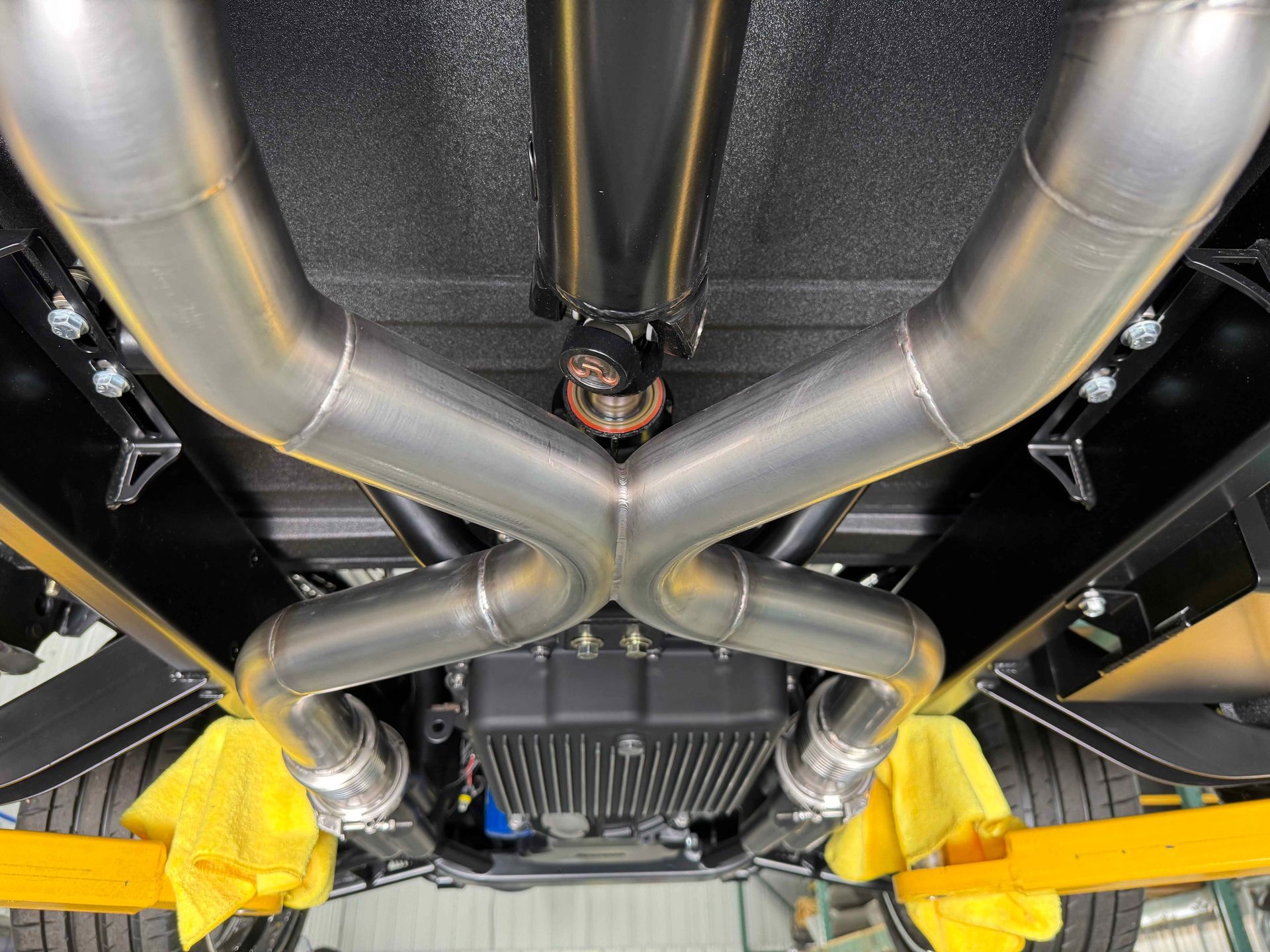 Underside of a car with polished exhaust pipes and bright yellow suspension components in a workshop