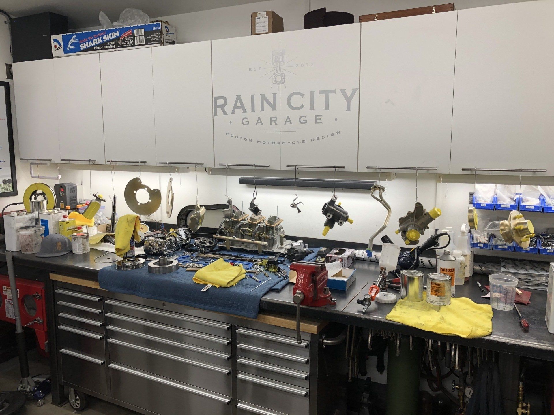 Automotive workbench with tools, parts, and drawers under a Rain City Garage sign