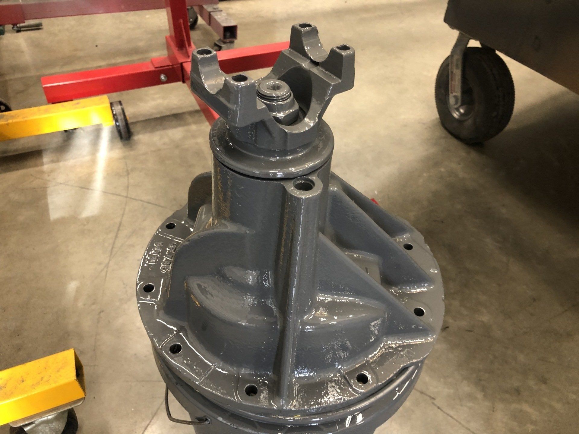 Gray metal mechanical component mounted on a wheeled cart in an industrial workshop, with a red frame in the background