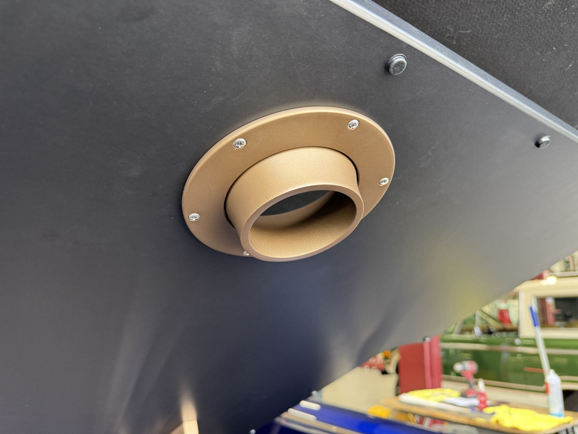 Close-up of a tan circular vent or pipe fitting on a dark gray metal panel.