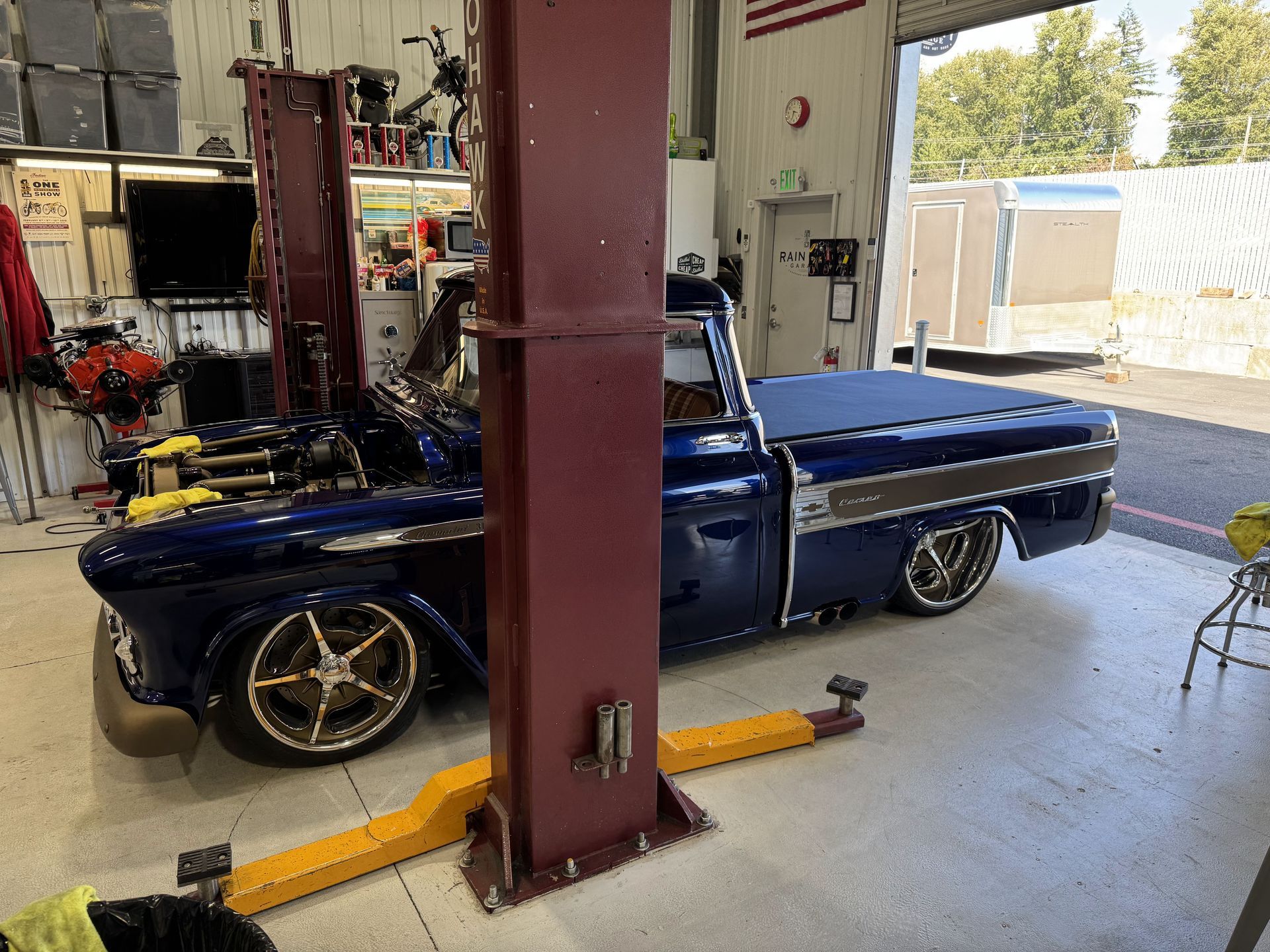 Blue classic car on a lift inside an auto shop, viewed around red support posts.