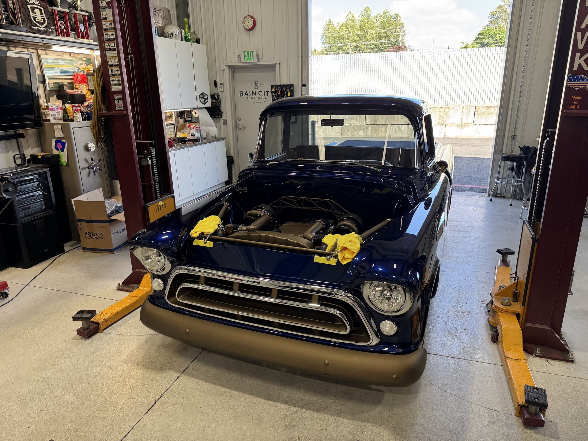 Classic black pickup truck in a garage, front end partially disassembled on a lift or jack stands.