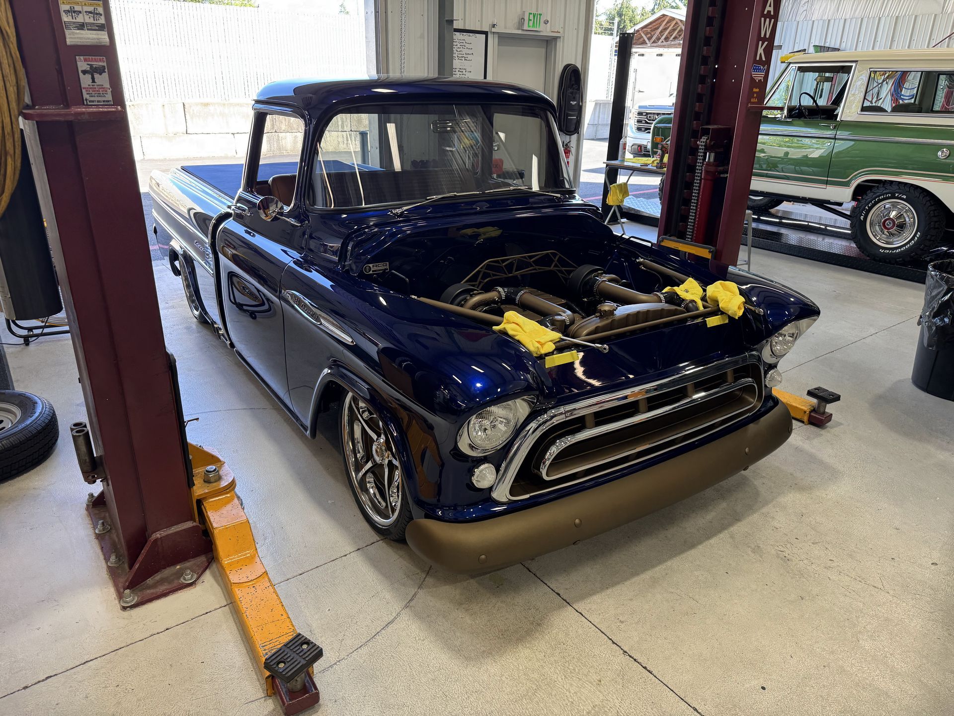 Classic black pickup truck in a garage, front view, with a gold front bumper and hood open