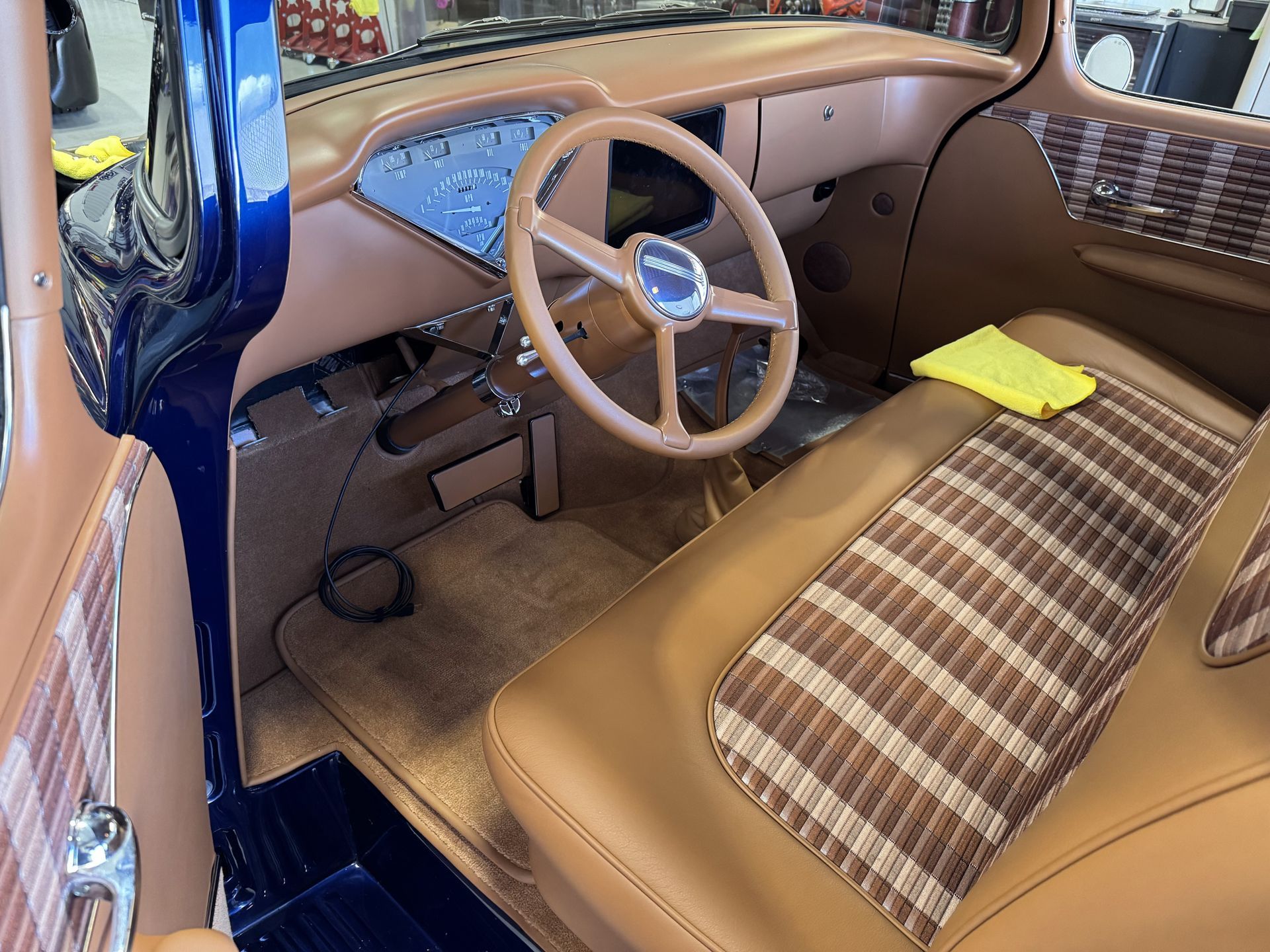 Vintage car interior with tan bench seat, wood steering wheel, and blue dashboard trim