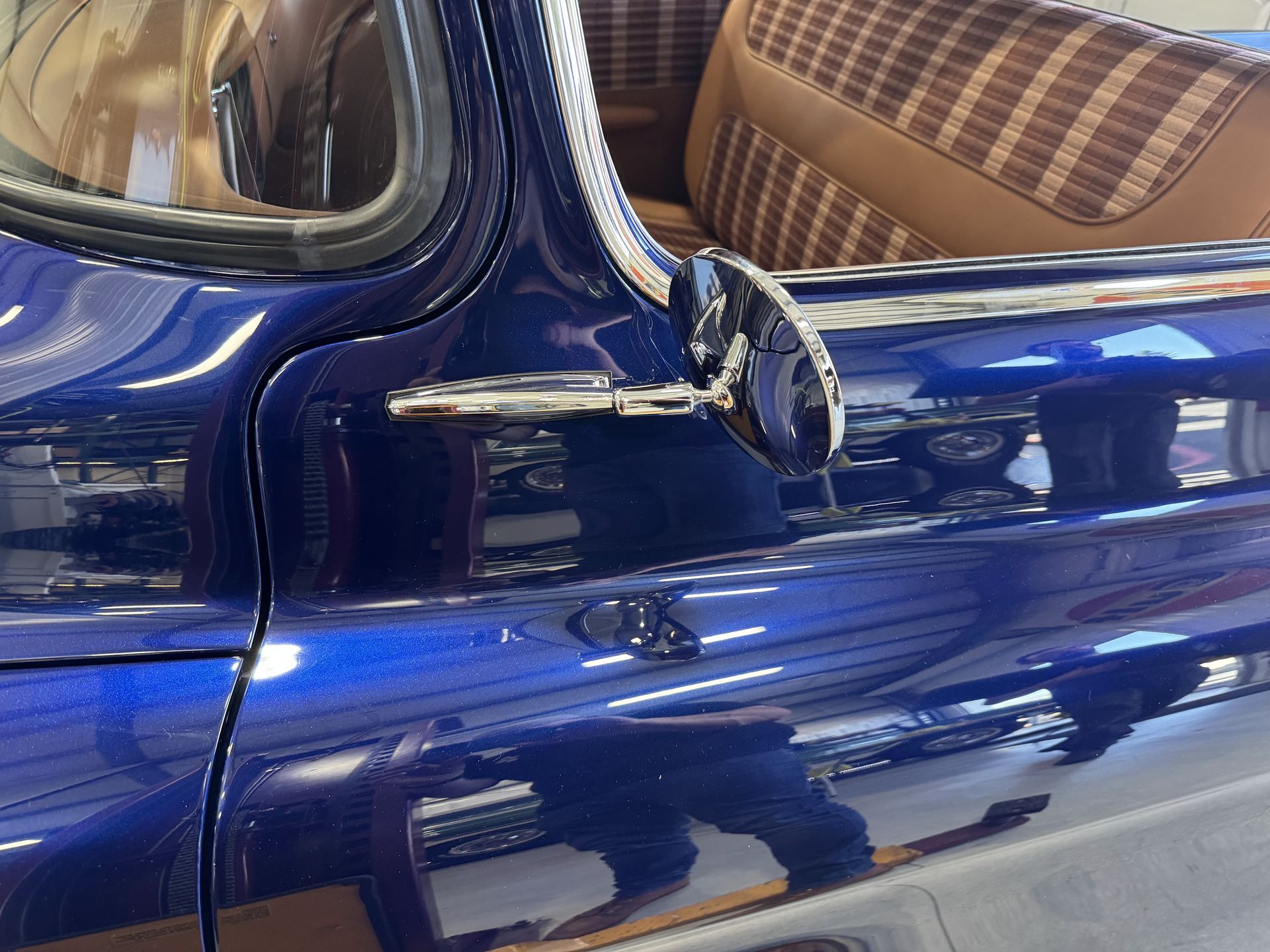 Close-up of a blue vintage car door with chrome trim and tan plaid interior visible through the window