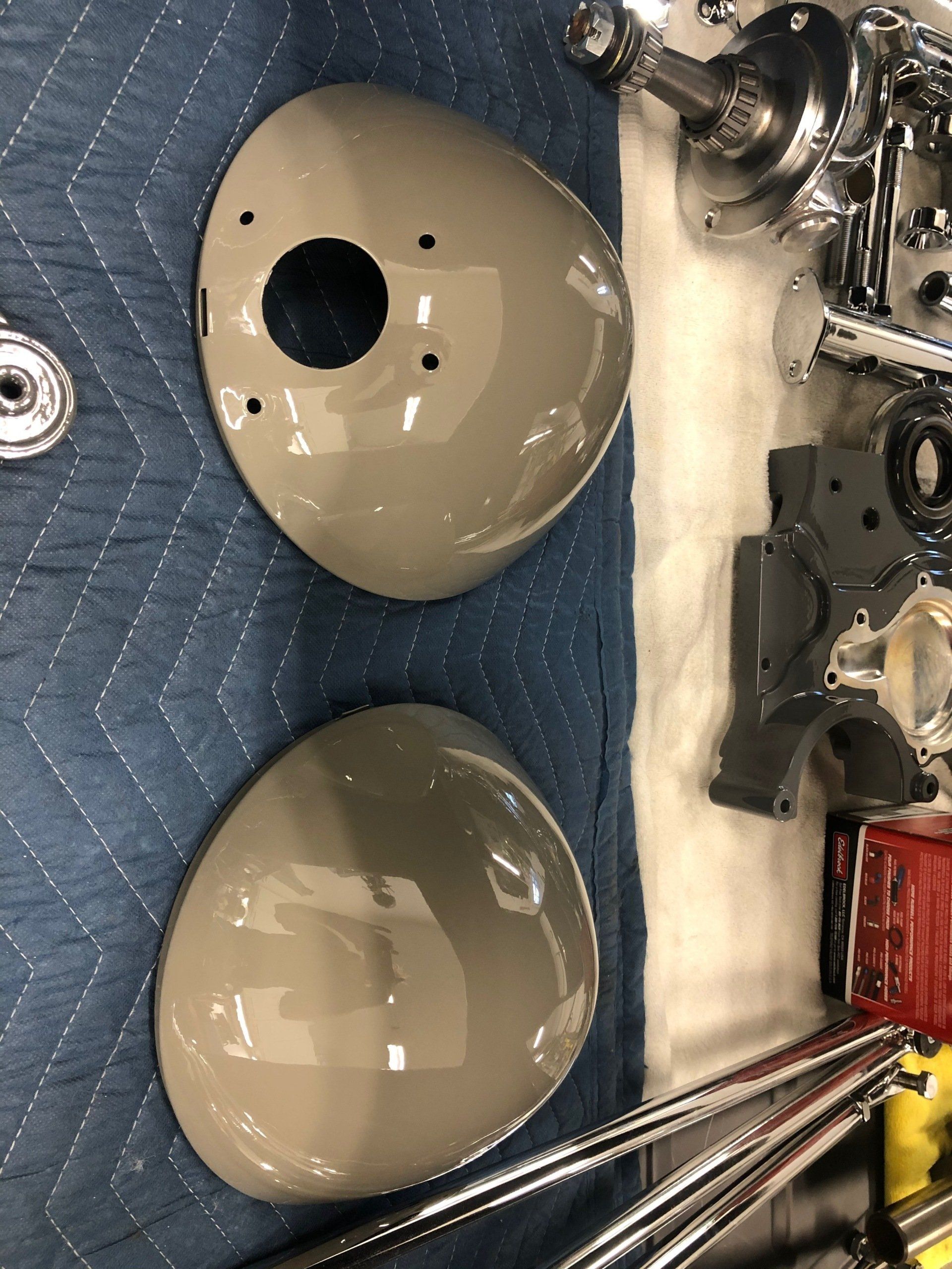 Two beige helmet shells on a quilted mat beside assorted metal hardware and tools.