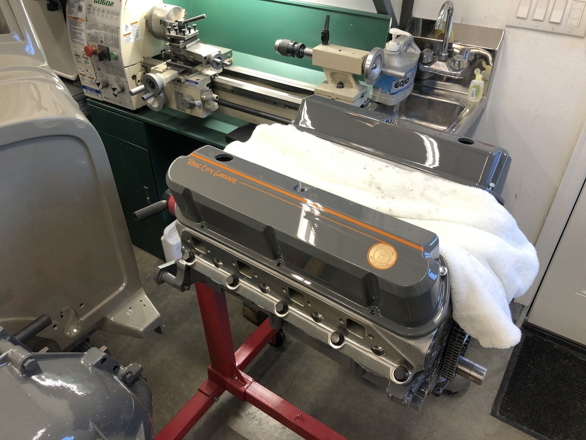 Workshop with a green industrial machine and a metal engine block on a red stand, covered by a white cloth.
