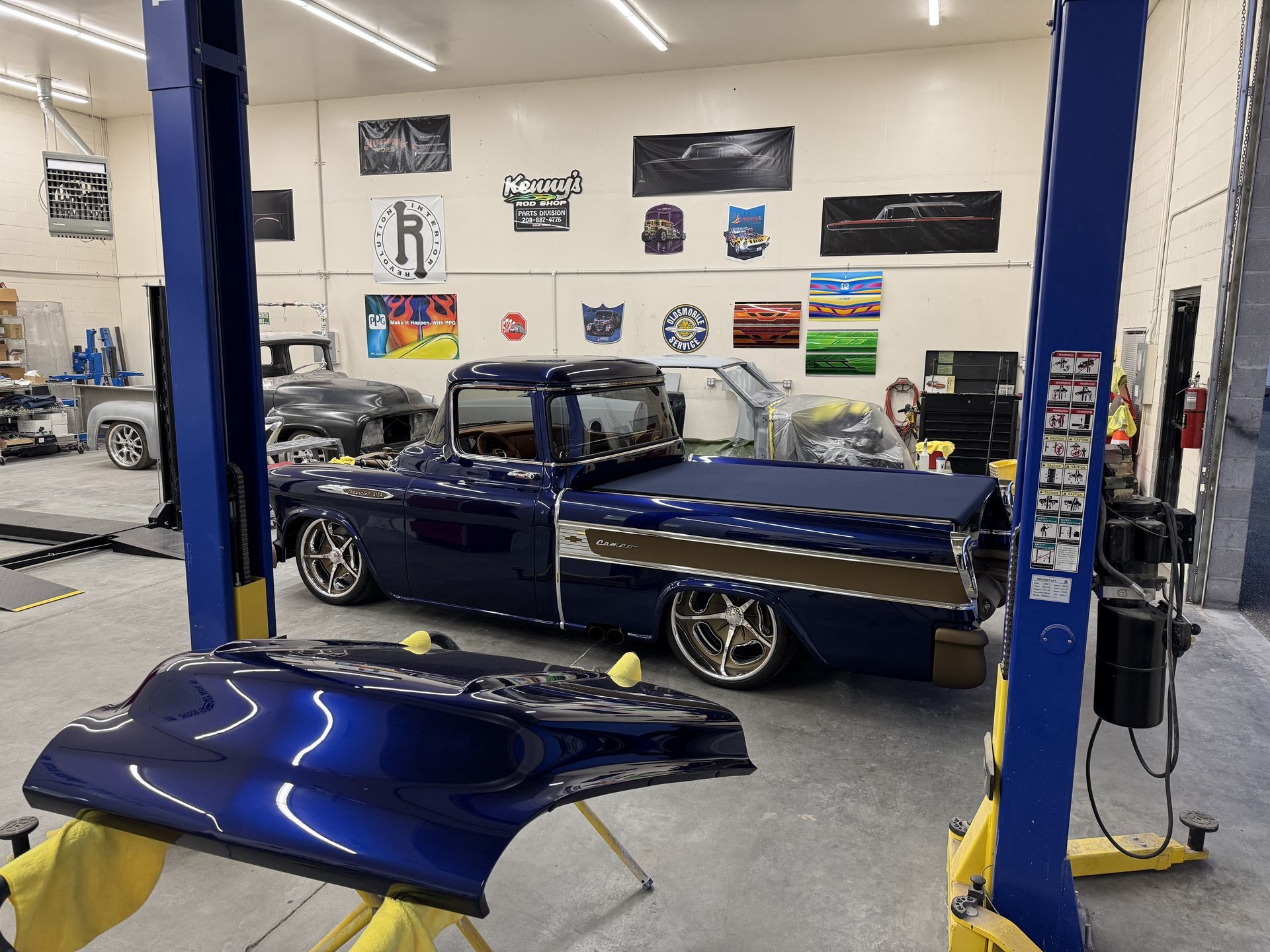 Classic blue car in a garage lift bay with a detached hood in the foreground