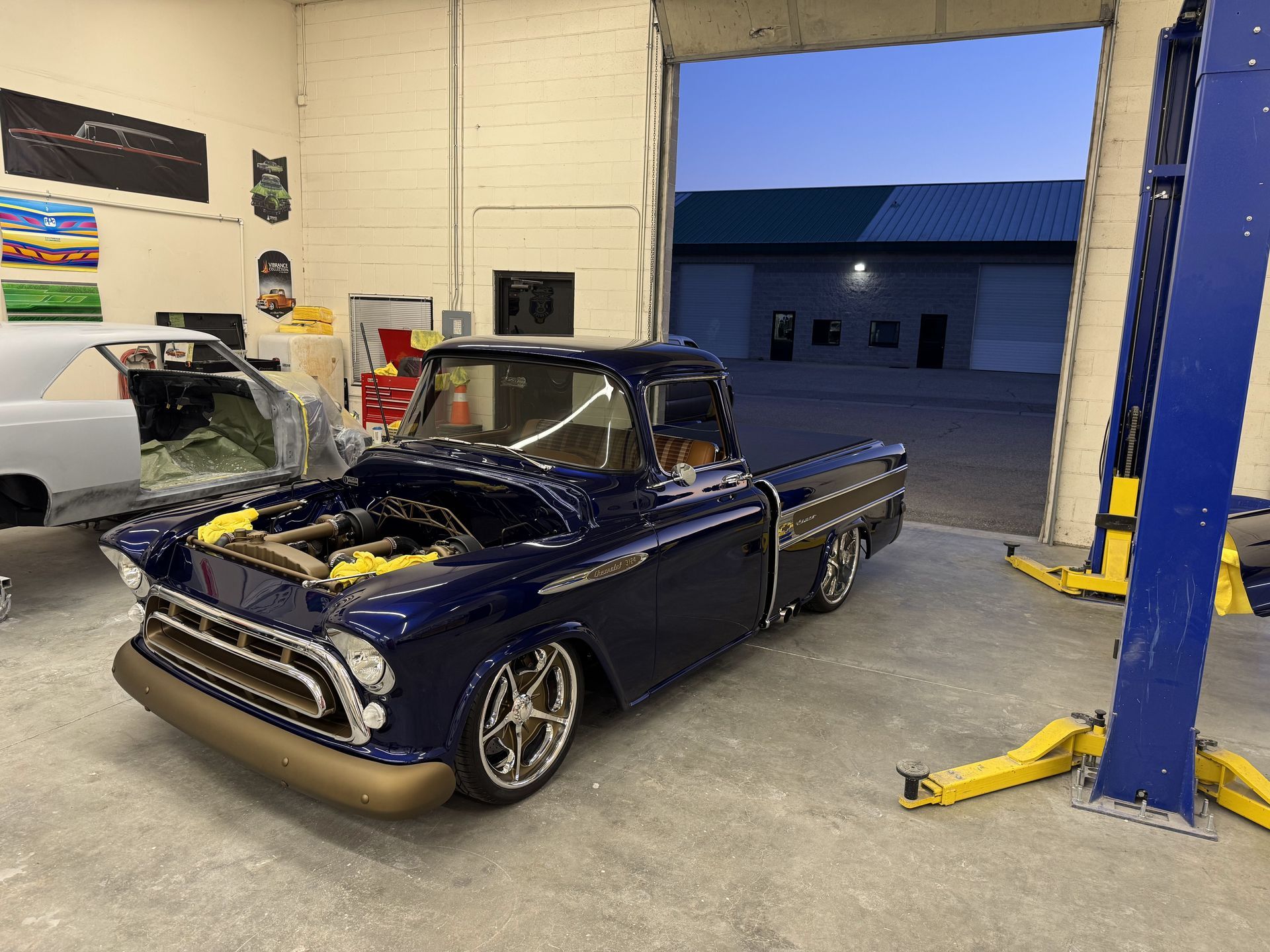 Lowrider pickup with hood open in a garage beside a blue vehicle lift