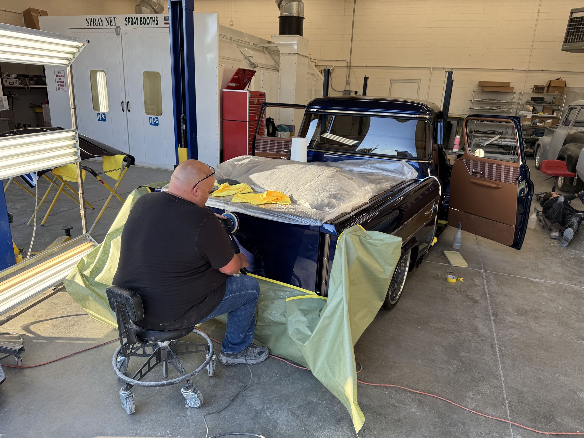 Person repairing a blue car in a workshop, with tape and plastic sheeting covering the body.