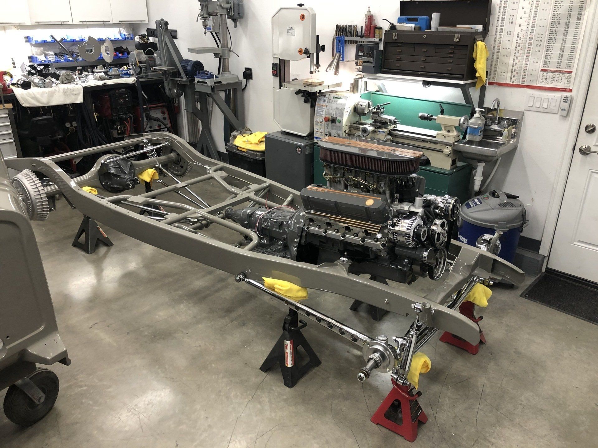 Automotive chassis in a workshop on jack stands, with engine parts and tools nearby