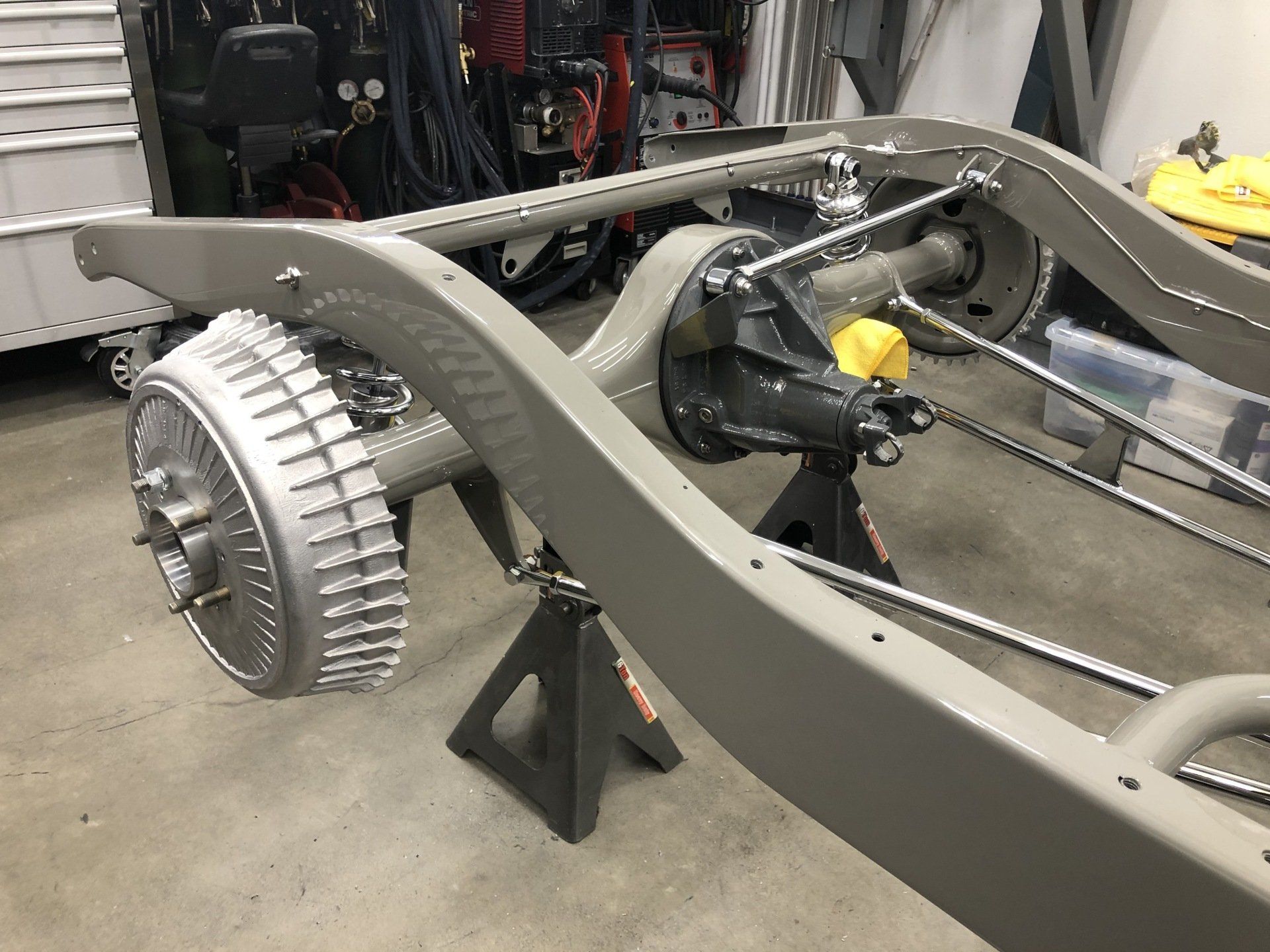 Partially assembled car chassis with gray frame, rear wheel hub, and exposed mechanical components in a workshop