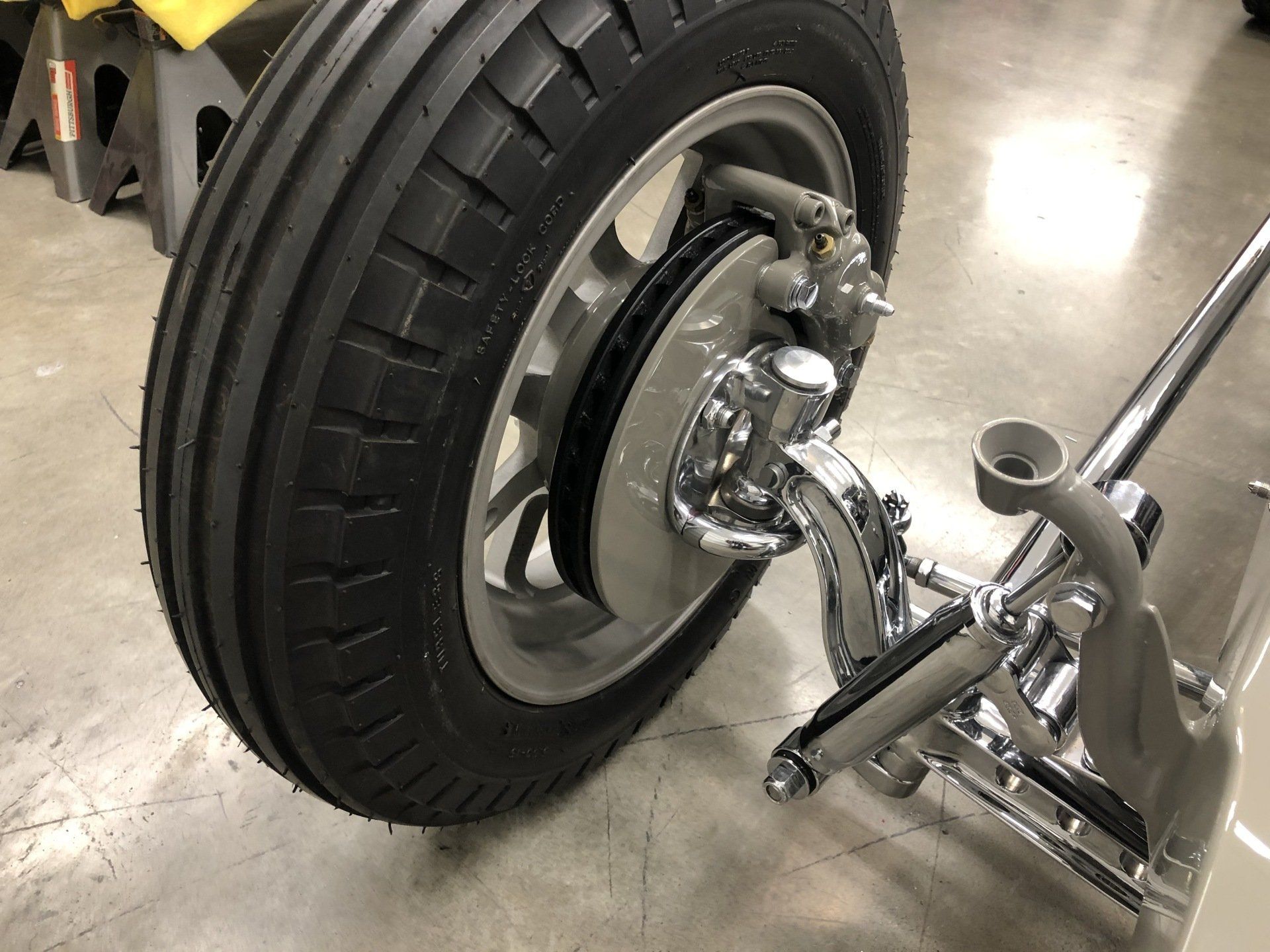 Close-up of a car wheel and brake assembly being inspected on a jack in a garage.