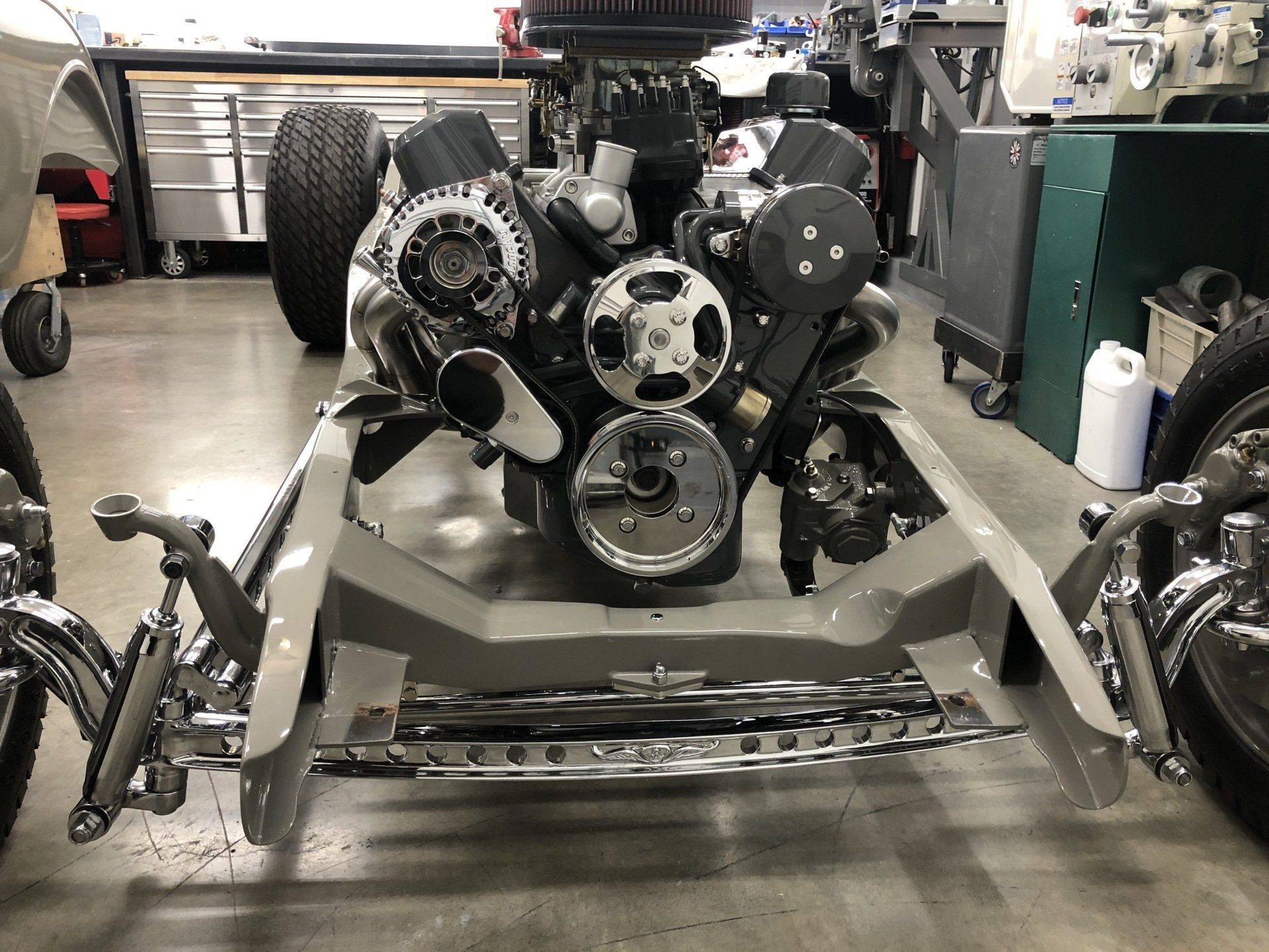 Car chassis in a workshop with exposed engine, belts, and wheels on a lift or stand
