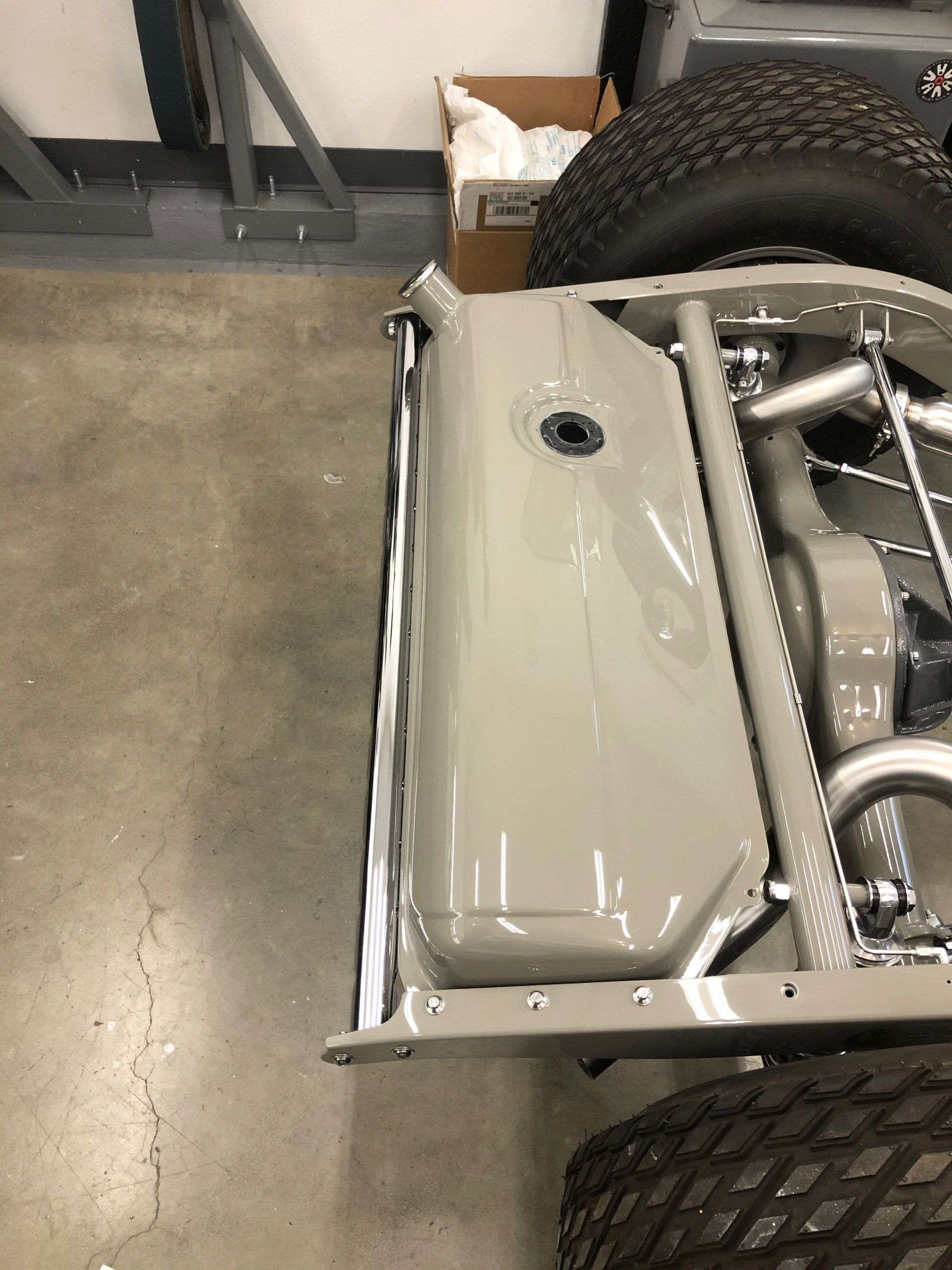 Beige vehicle chassis with exposed frame and large tires in a garage on a concrete floor