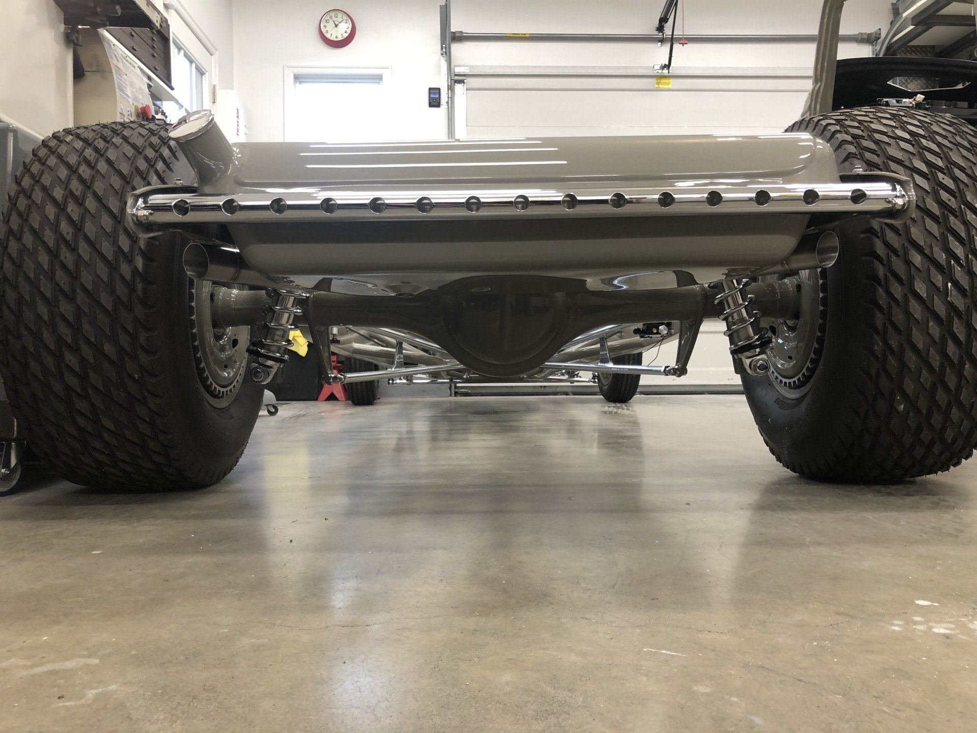 Low-angle view of a lifted off-road vehicle’s rear axle and large tires in a garage