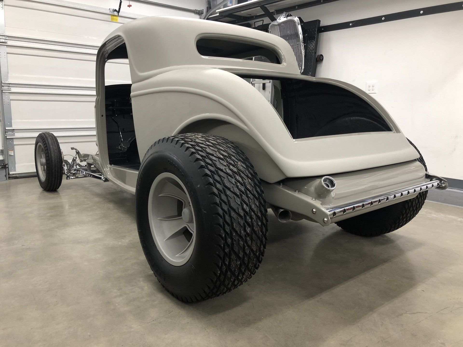 Custom light-gray hot rod chassis in a garage, front three-quarter view with large rear tires and exposed engine.