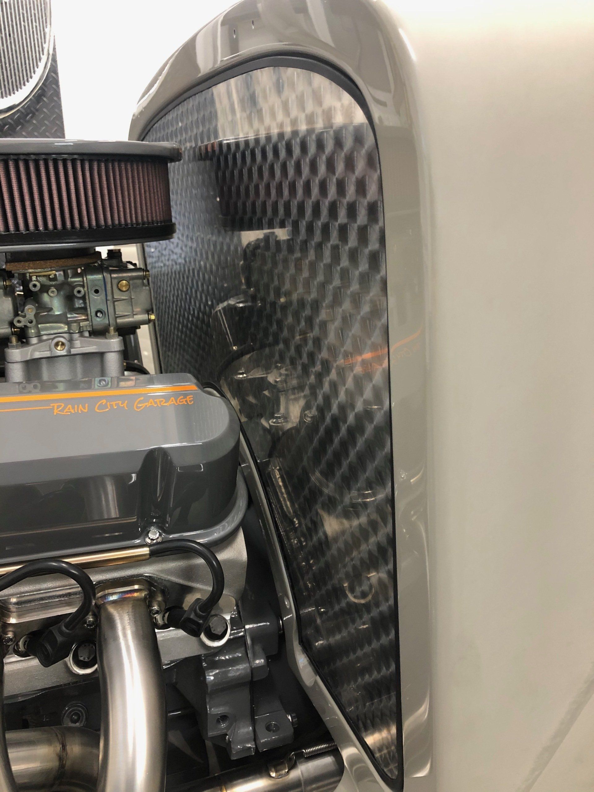 Close-up of a small engine with a carbon-fiber panel and chrome exhaust pipe