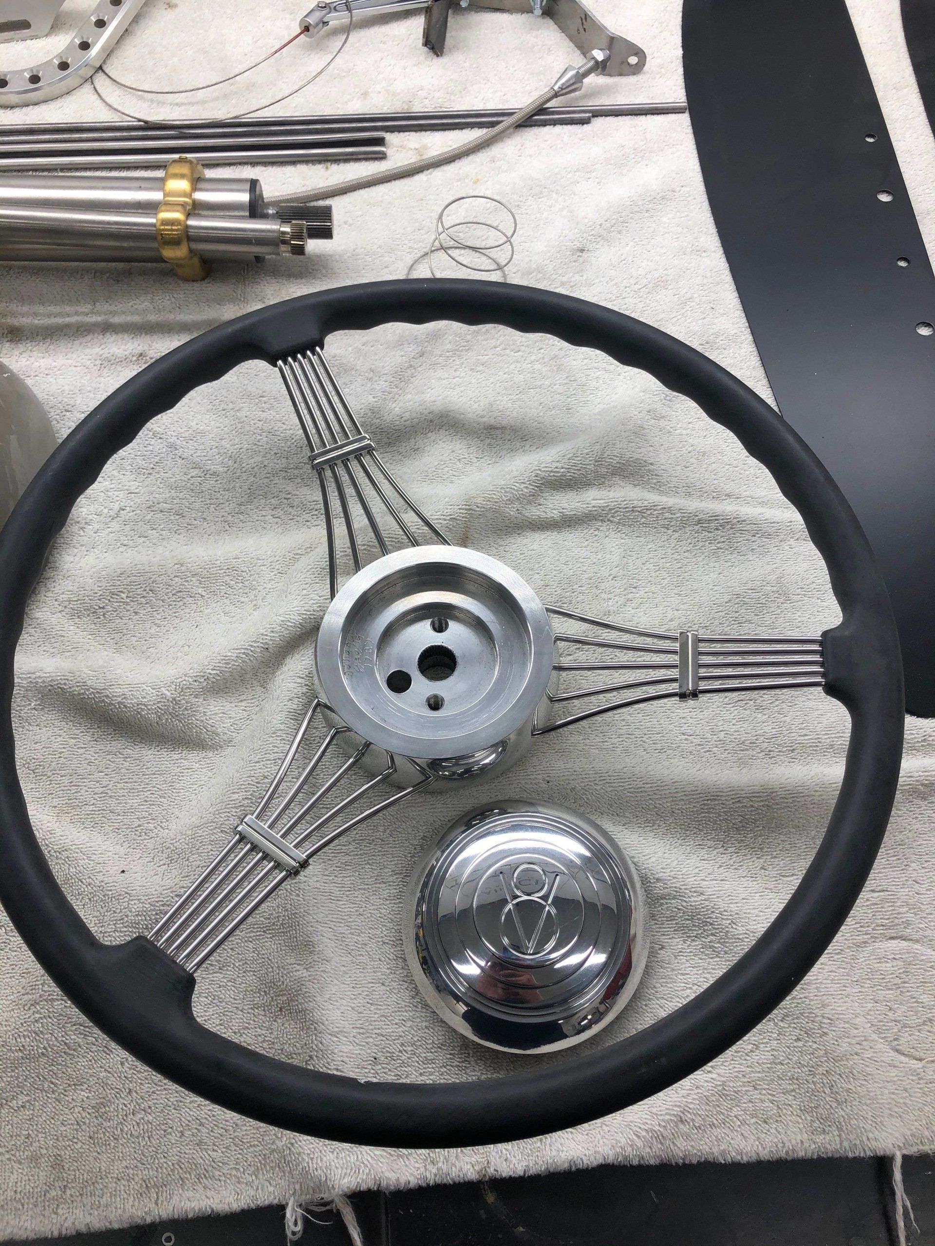 Black steering wheel with metal hub, chrome horn cap, and cables on a gray cloth work surface