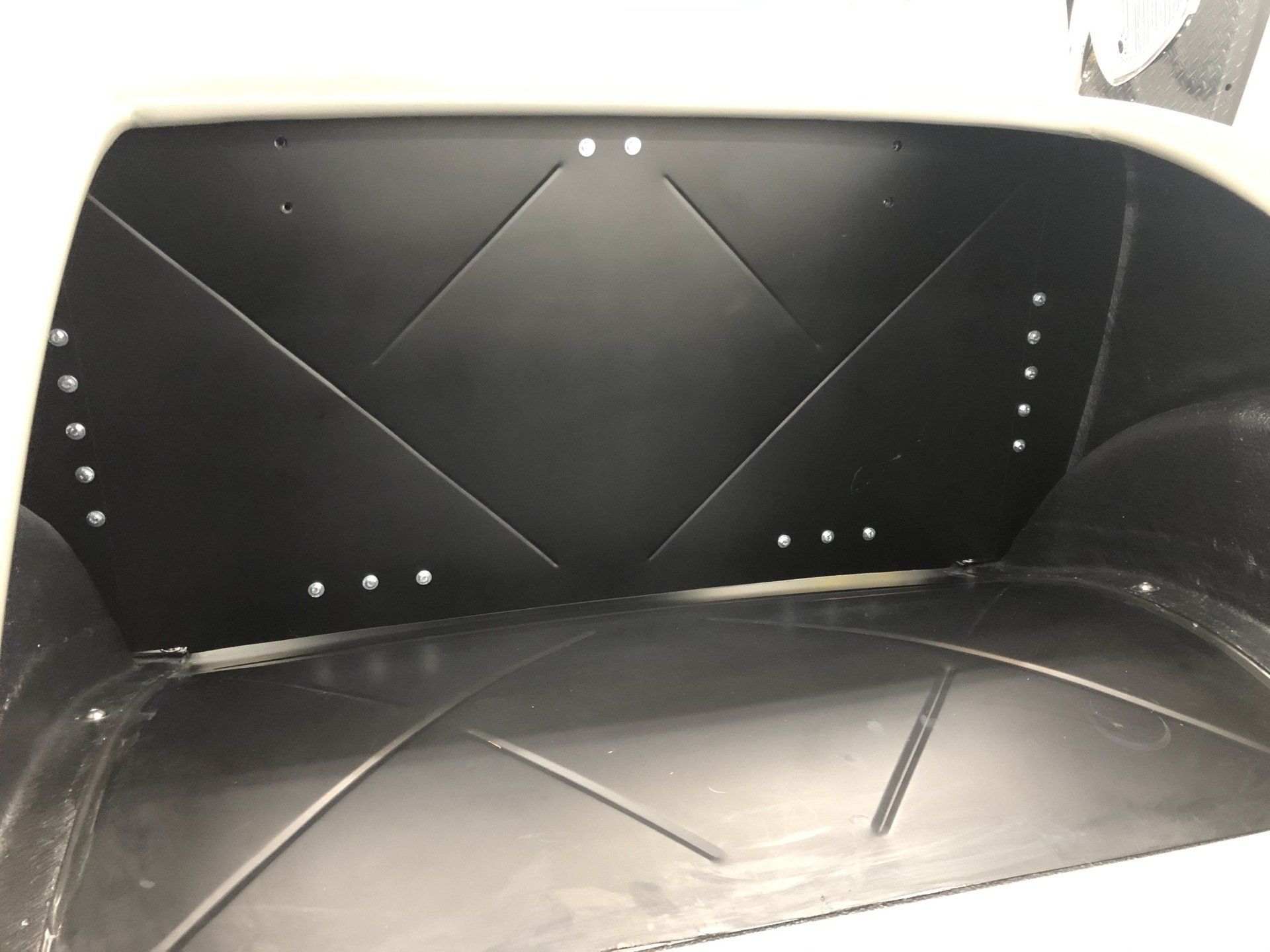Black padded storage compartment with rivets and quilted panels, viewed from the inside.