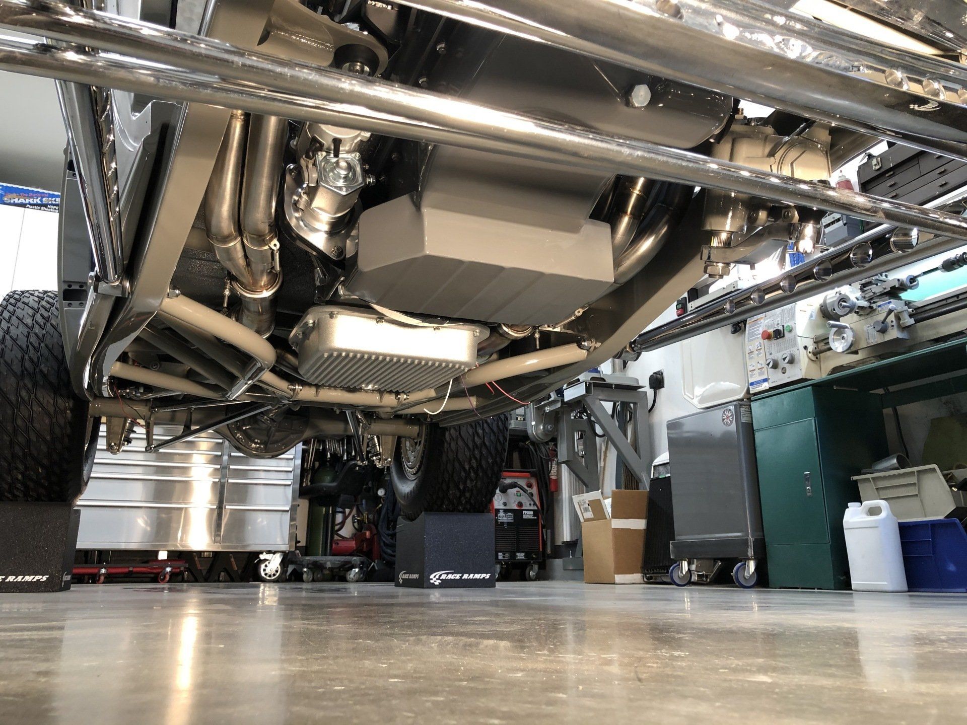 Low-angle view of a shiny industrial machine beneath metal pipes in a workshop or factory setting