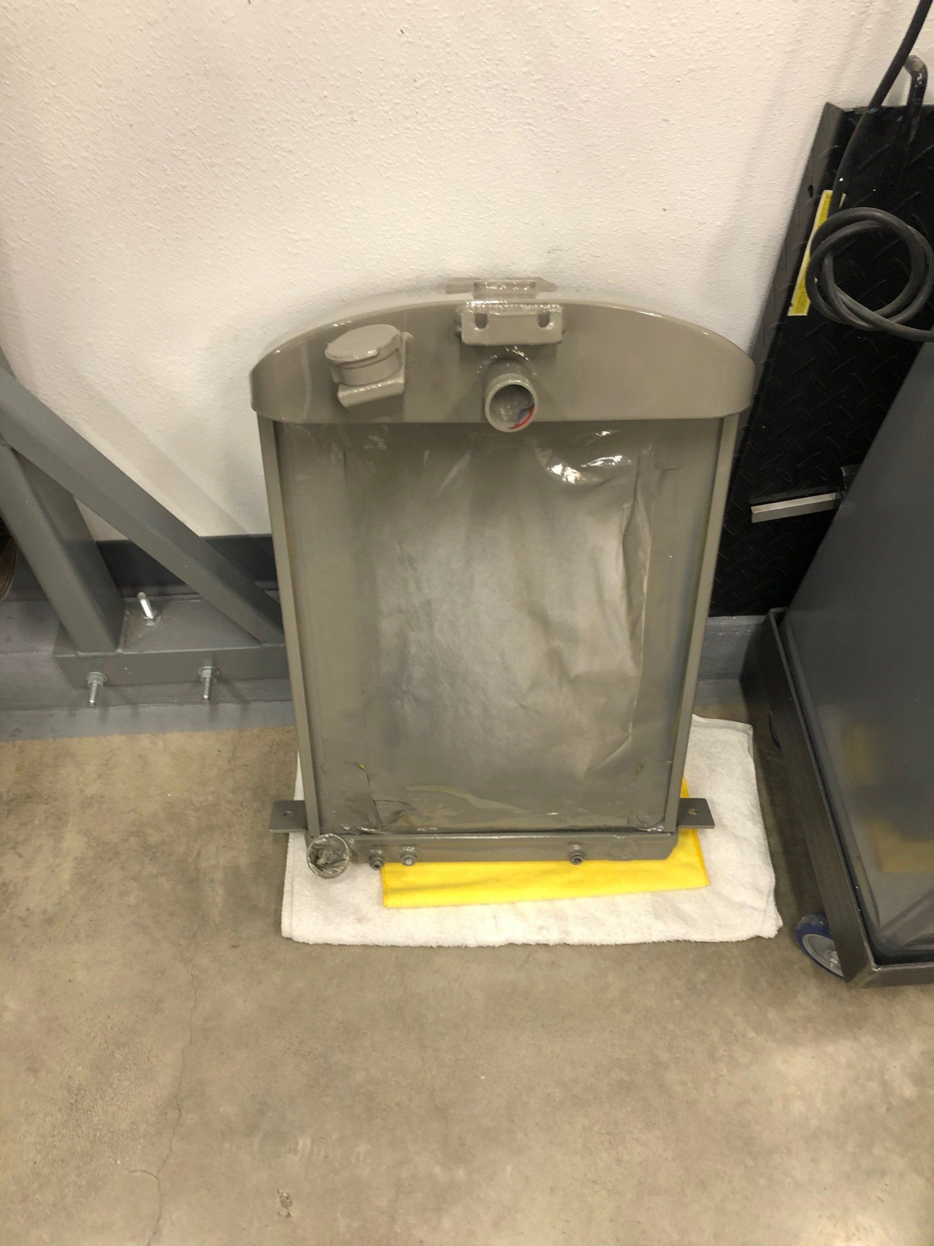 Metal utility cabinet with a yellow base cover, sitting on a floor in an industrial room.