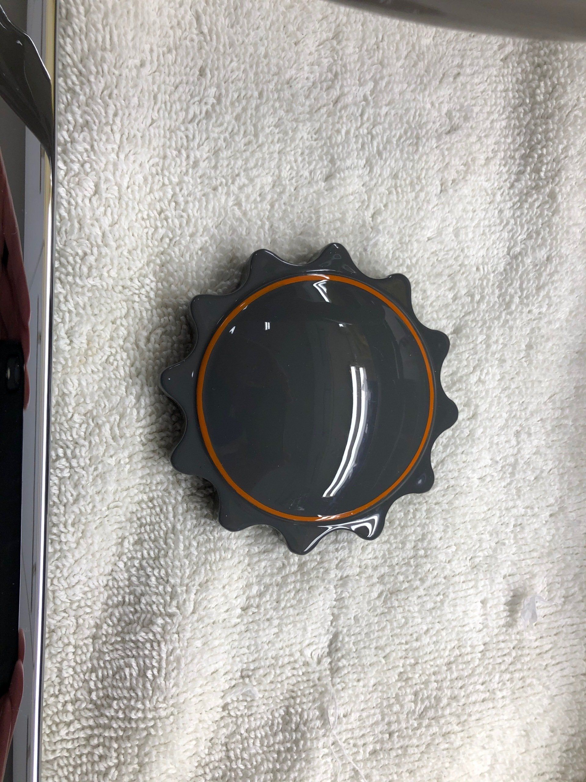 Black round watch with orange rim on a white towel, viewed from above.