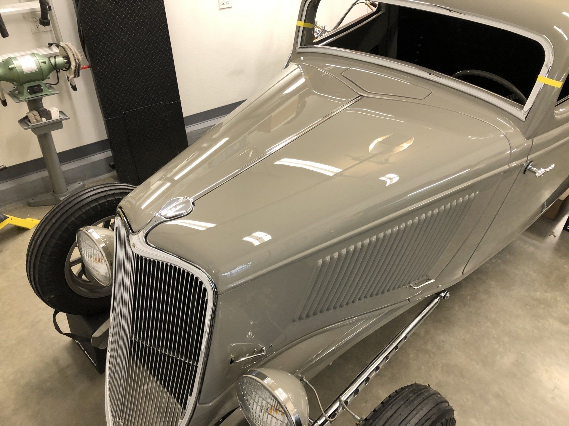 Gray vintage hot rod car in a garage, front-left view with chrome grille and exposed wheels