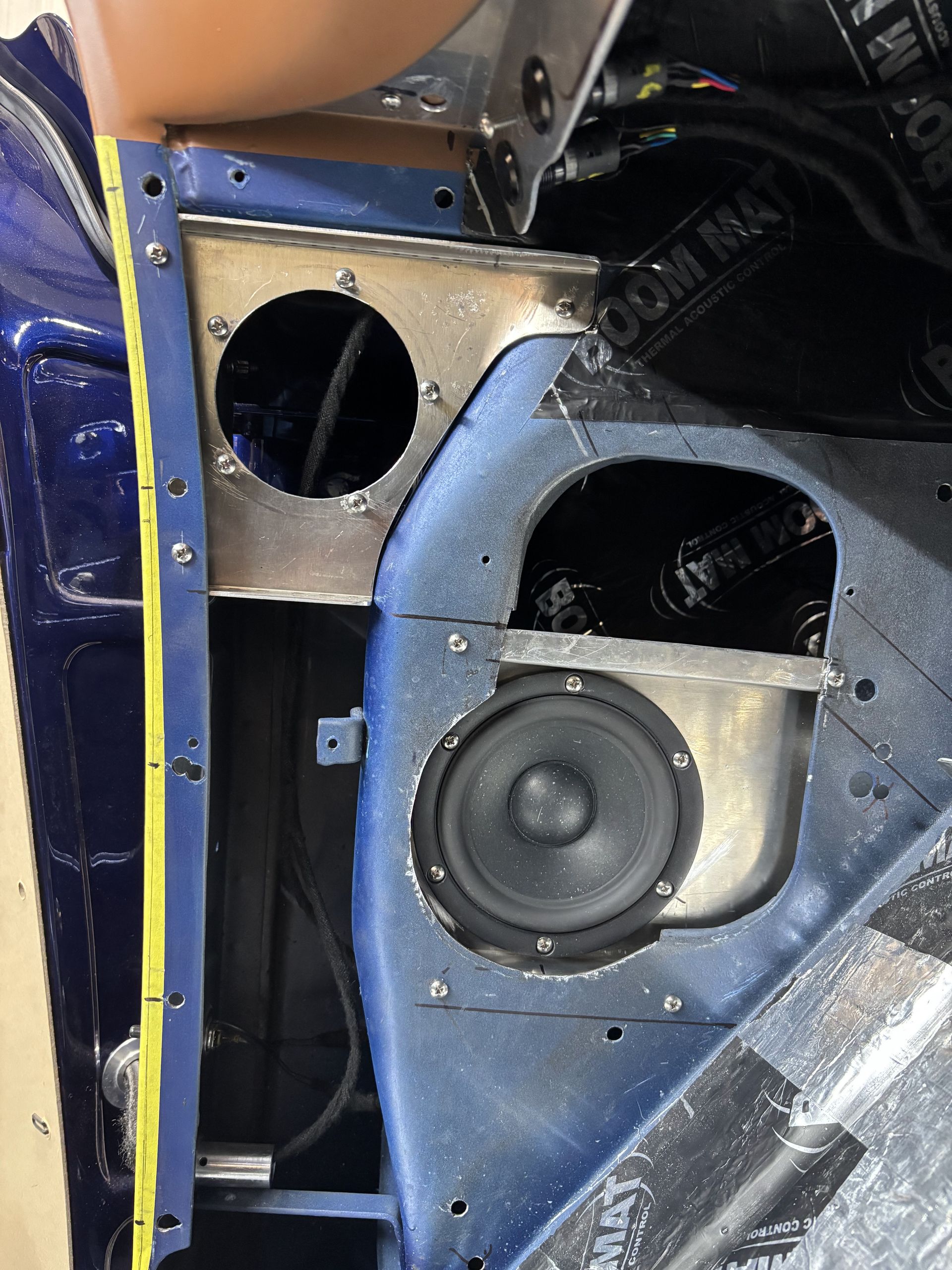 Blue car door interior with exposed speaker openings and a mounted black speaker.