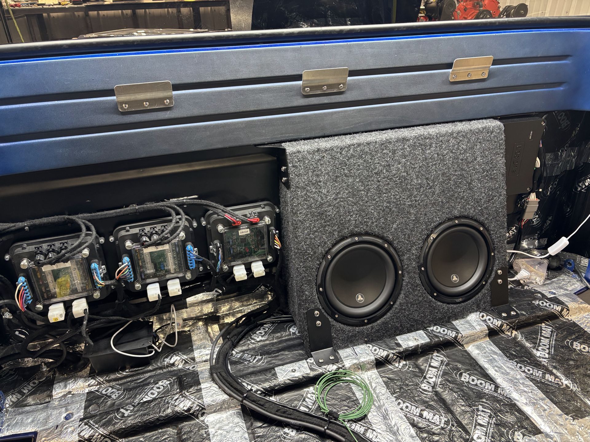 Car audio subwoofer enclosure and amplifier setup in a truck trunk, with exposed wiring and components exposed