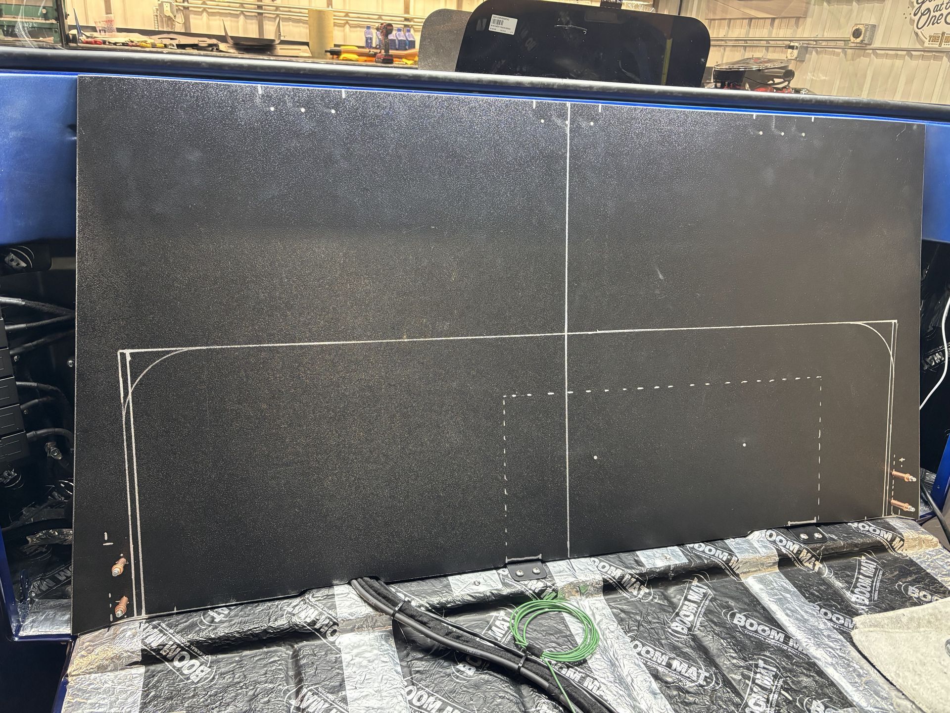 Black rectangular panel with white guide marks and a curved outline, mounted on a workbench in a workshop