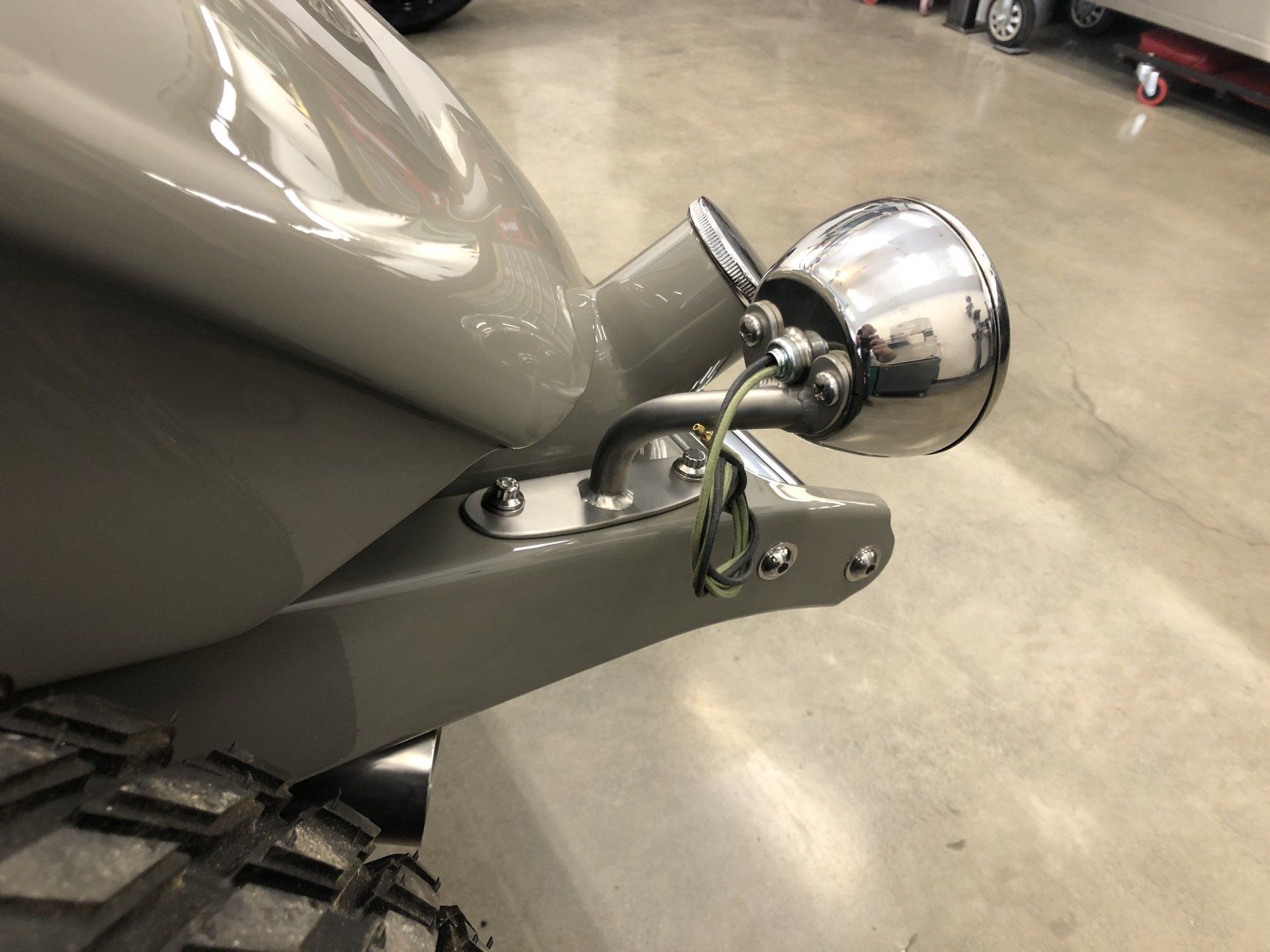 Chrome side mirror mounted on a gray vehicle body, close-up view