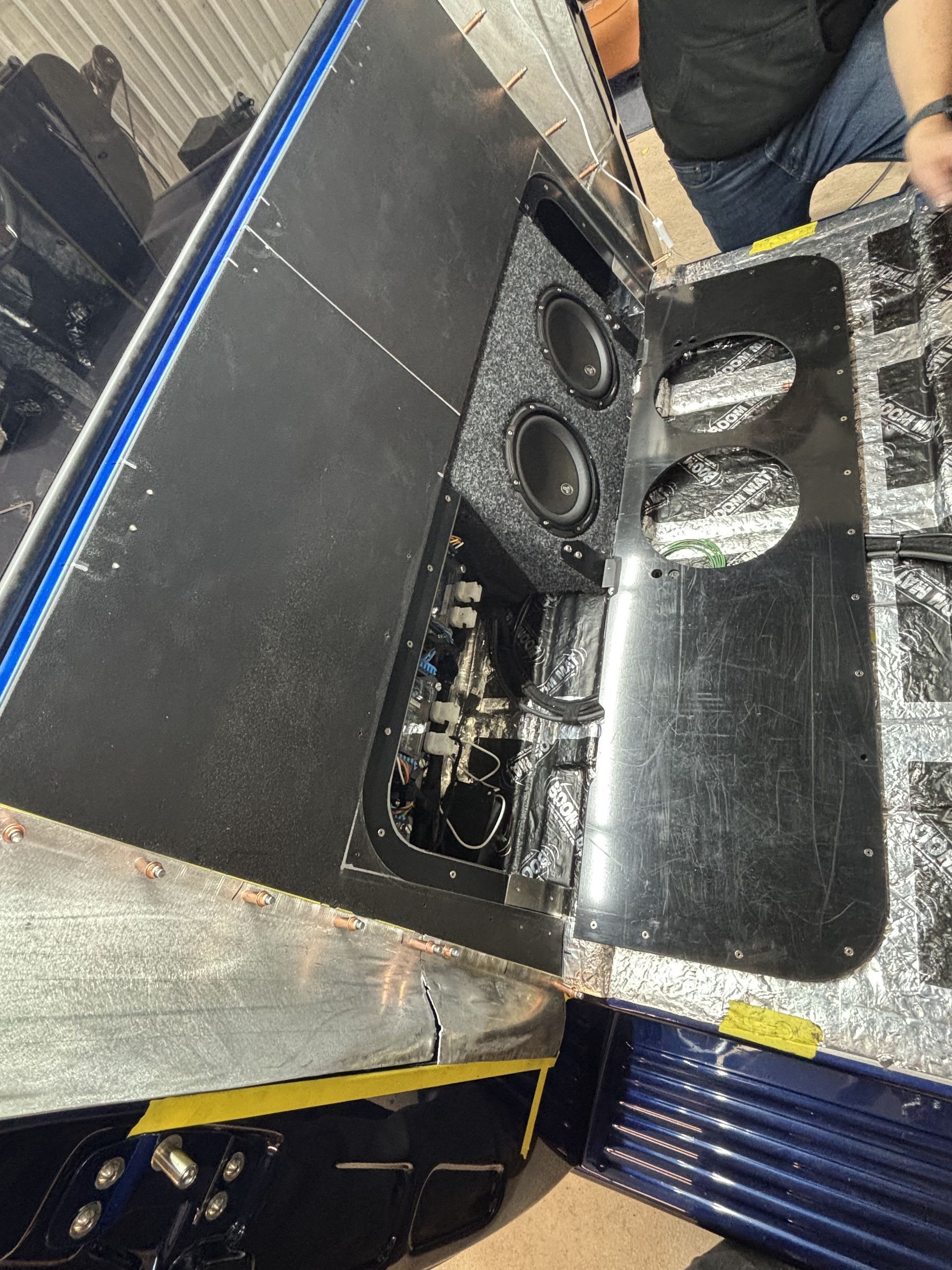Close-up of a black speaker cabinet with dual woofers and a cutout opening in a workshop setting