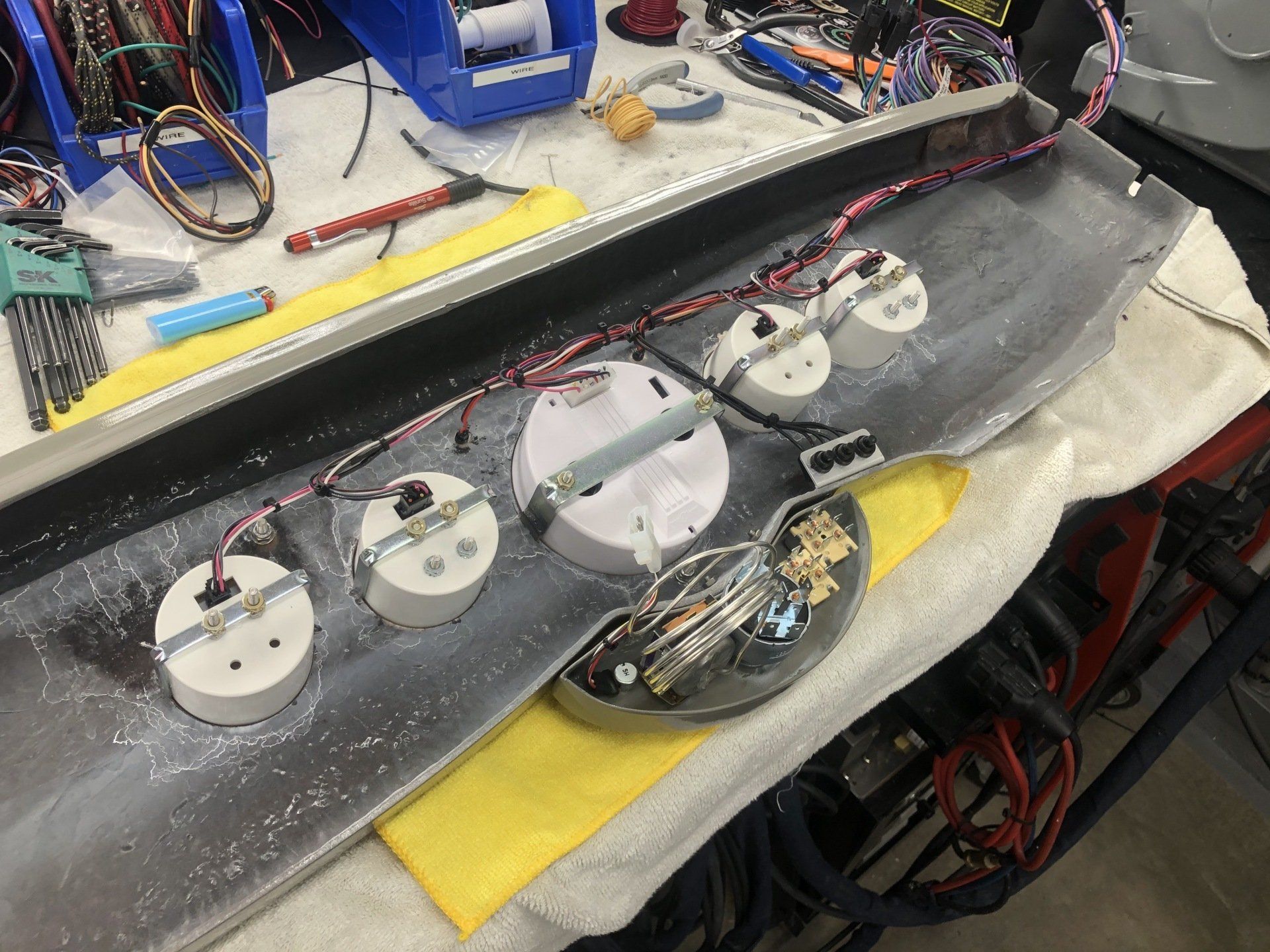 Electronic components and wiring laid out on a workbench for assembly, with several round modules on a black panel.