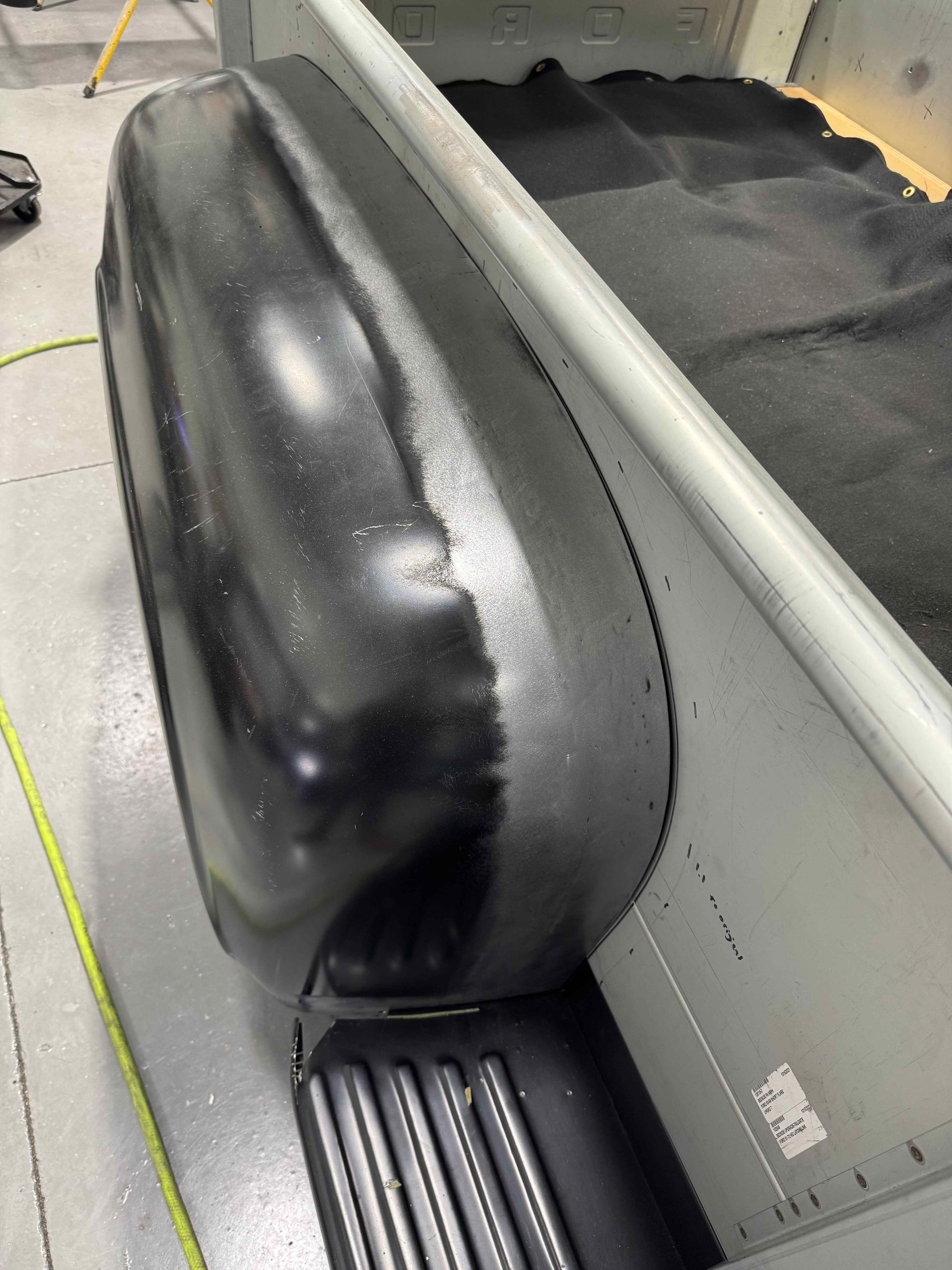 Black inflatable raft on a gray floor beside a white wall and black matting.
