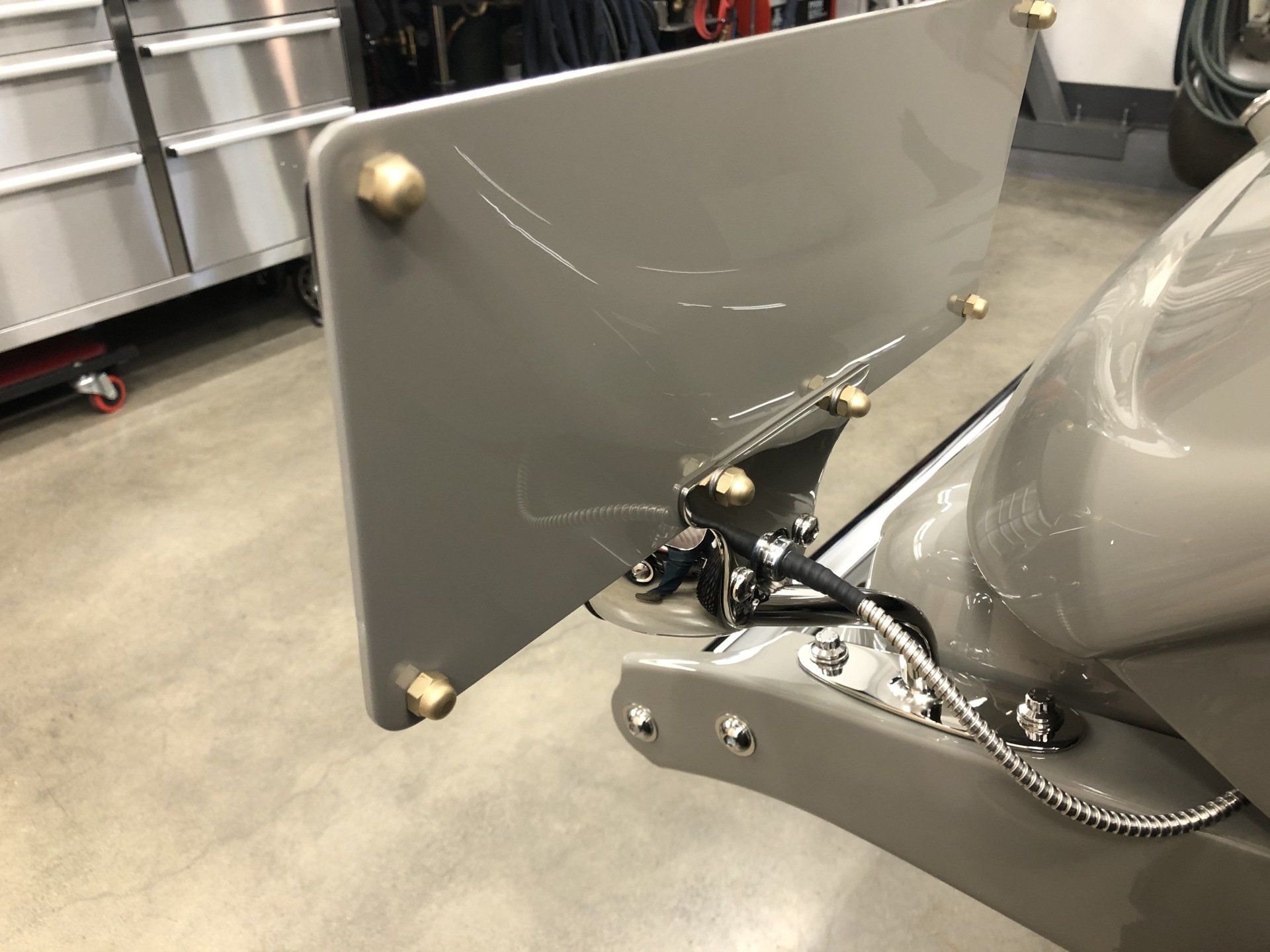 Gray rear-mounted wing/spoiler attached to a vehicle in a garage, with metal supports and chains.