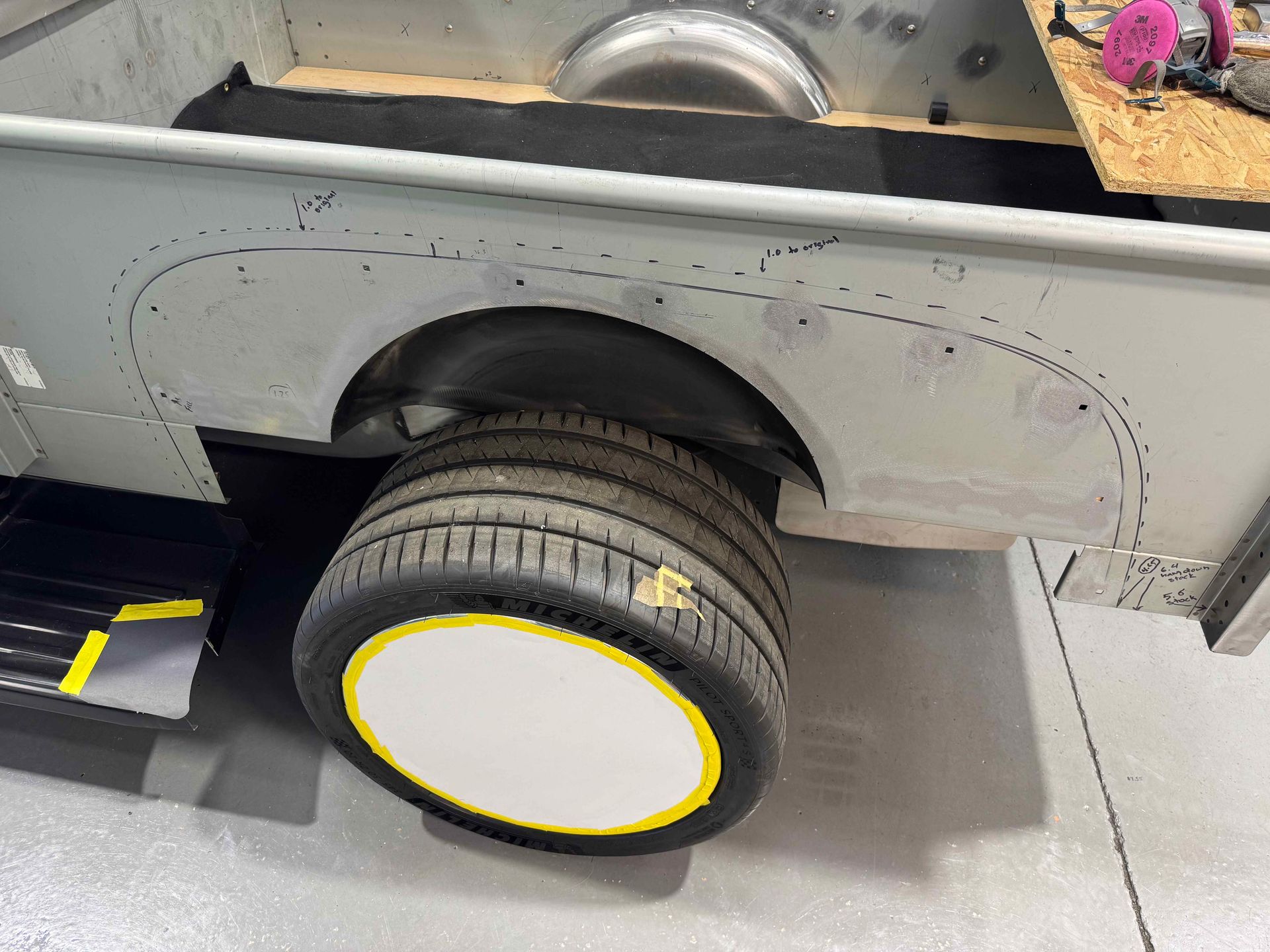 Silver truck side with a large white wheel and yellow trim parked indoors