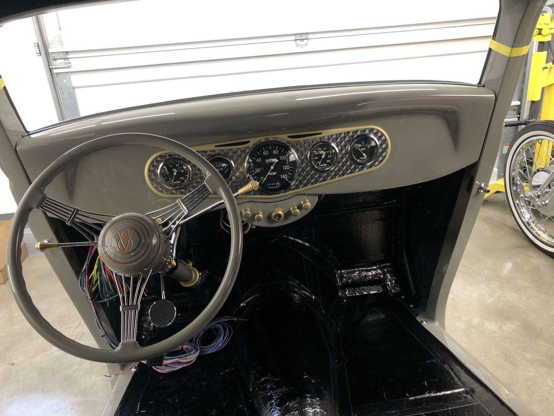 Vintage car interior with beige dashboard, large steering wheel, and black floor mat in a garage.