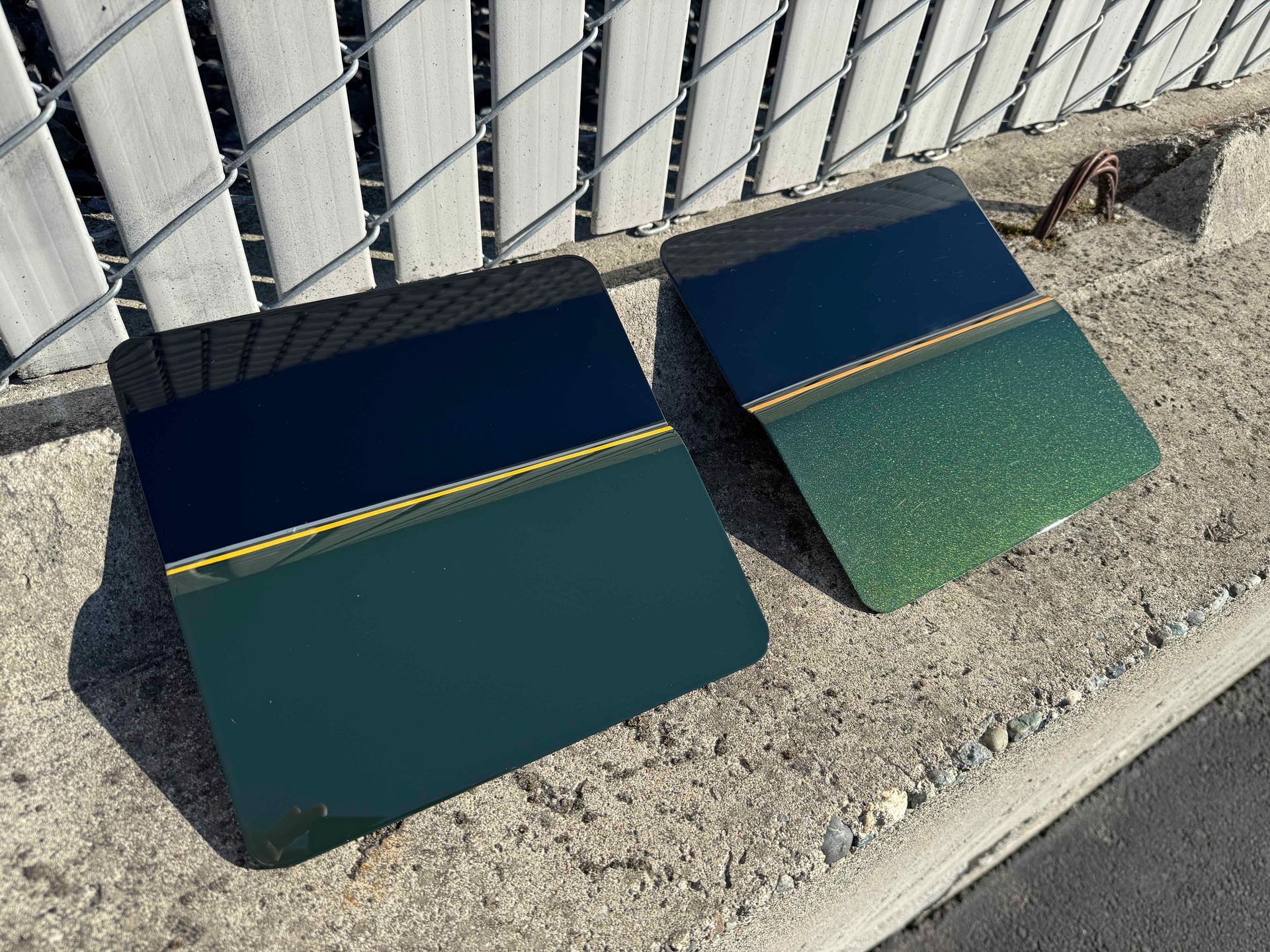 Two green and black metal panels leaning against a fence on gravel outdoors