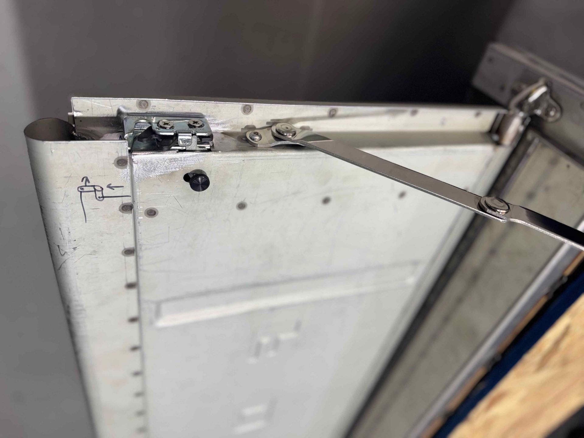 Metal cabinet door close-up with hinges and a support arm attached