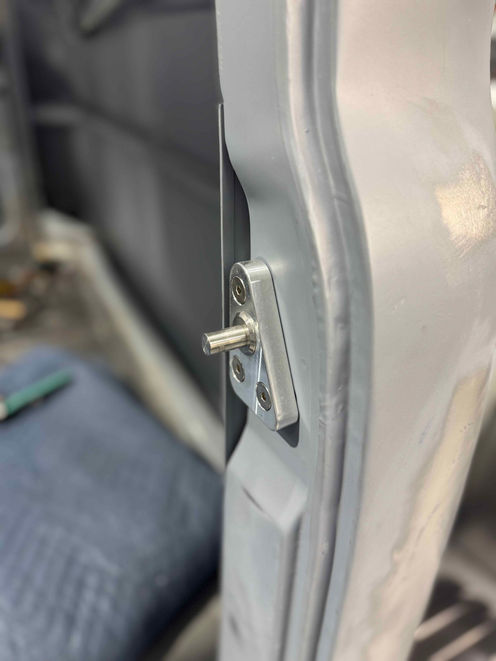 Close-up of a gray seat panel with a metal latch and protruding pin.