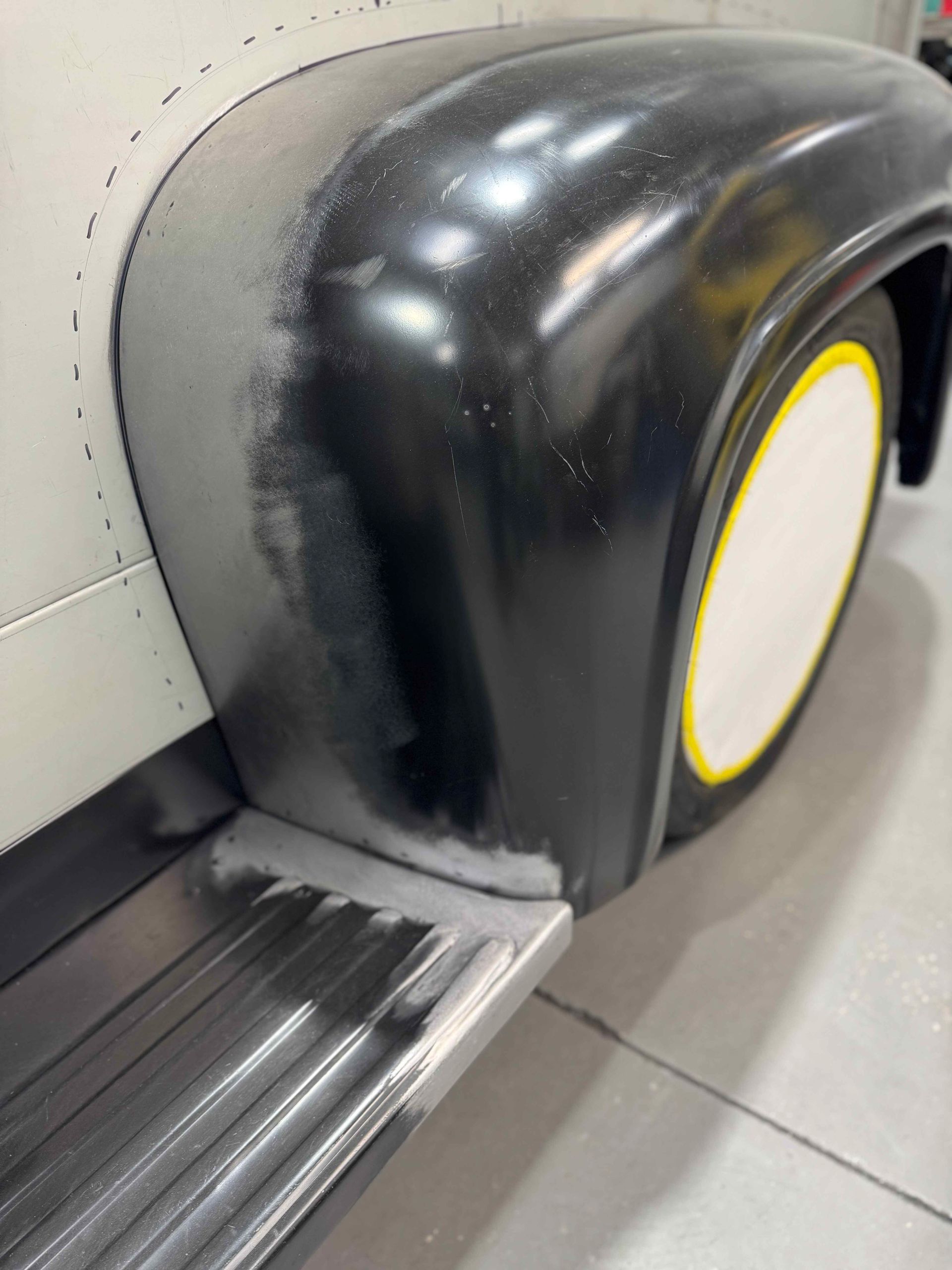 Black tactile paving at a subway platform edge beside a wall-mounted circular device with a yellow rim