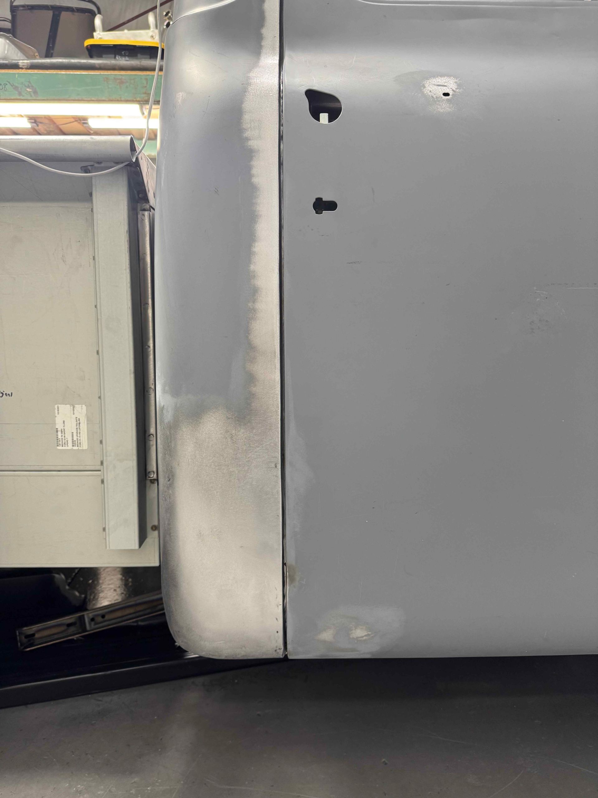 Close-up of a gray metal panel with two holes and a white vertical seam on the left.