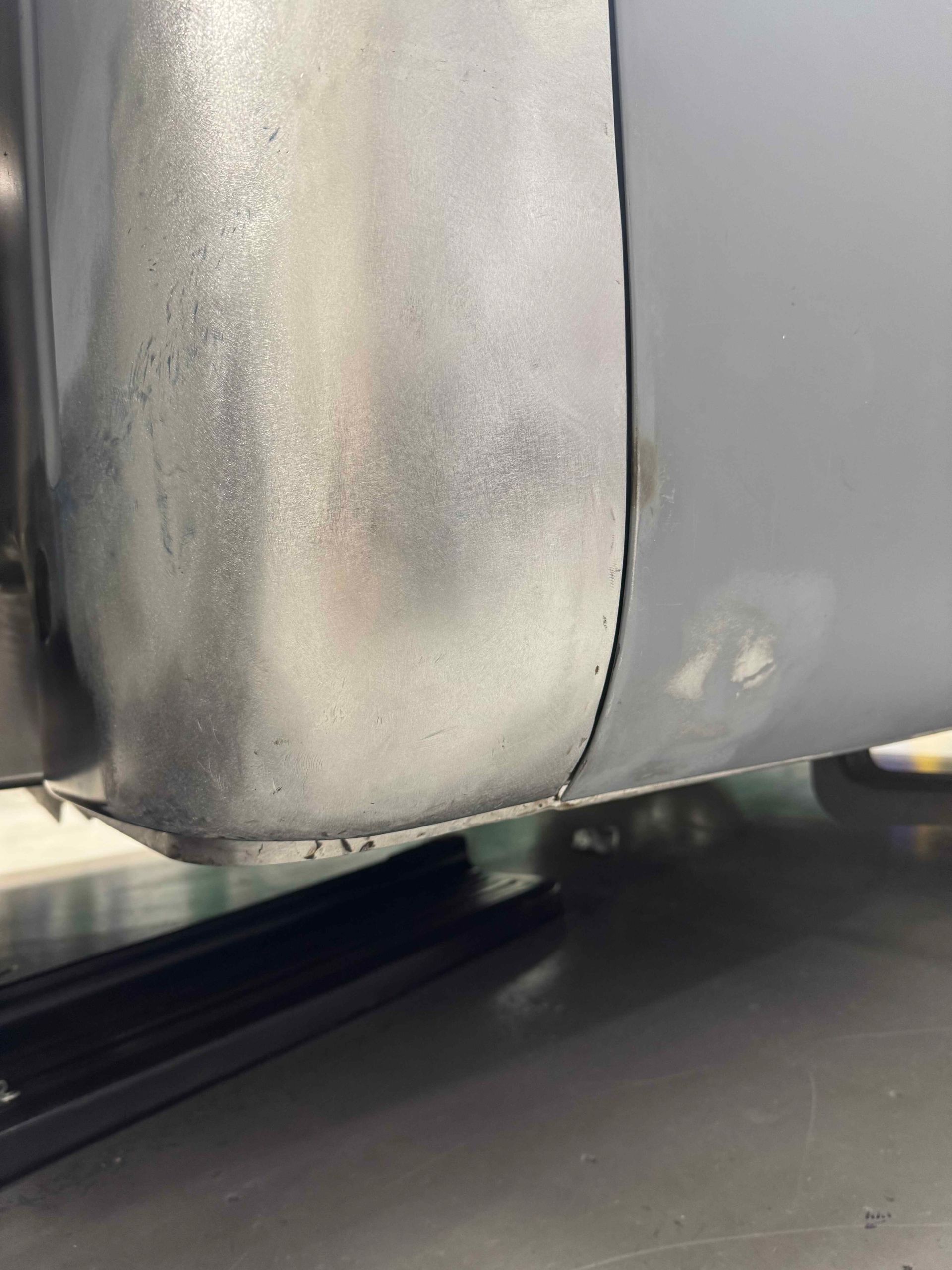 Close-up of a silver vehicle corner and black floor rail, with a scuffed gray panel beside it