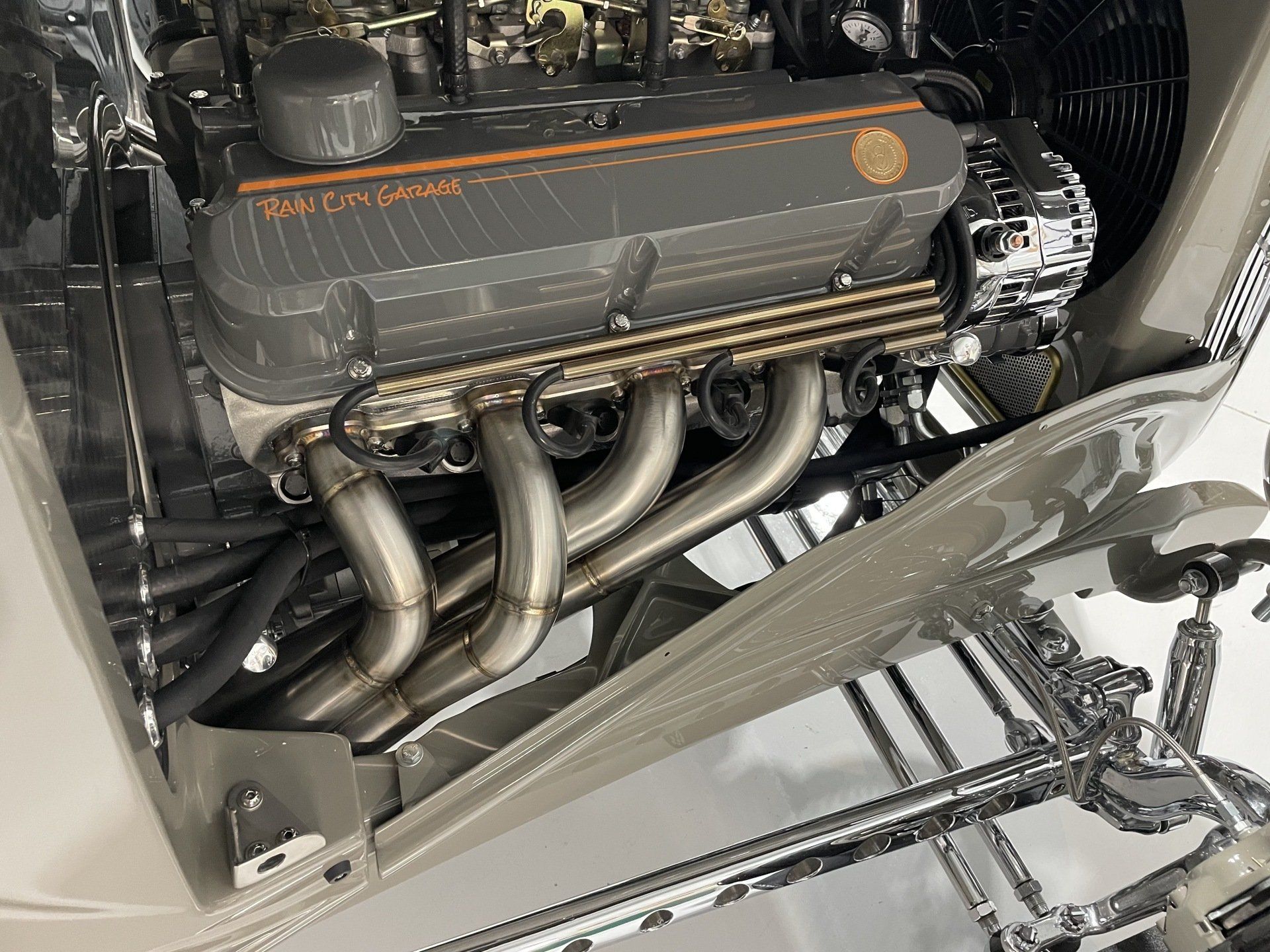 Custom chrome car engine with polished exhaust headers in a classic vehicle bay