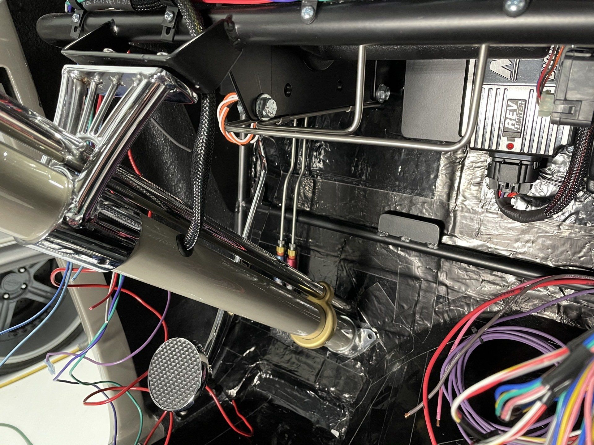 Close-up of a cluttered car interior with exposed wiring, metal tubing, and black insulation panels