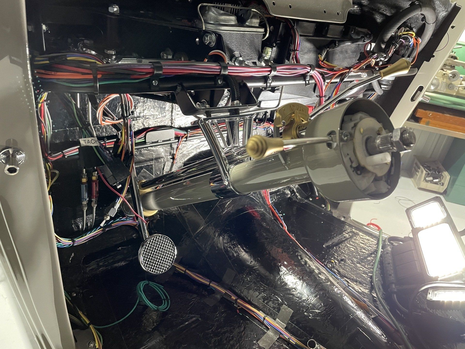 Interior of a vehicle dashboard with exposed wiring, metal components, and a steering shaft visible.